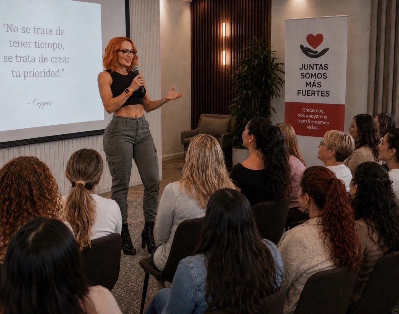 Mujer presentando en una conferencia con una pantalla que muestra una cita motivacional y un grupo de mujeres en la audiencia.