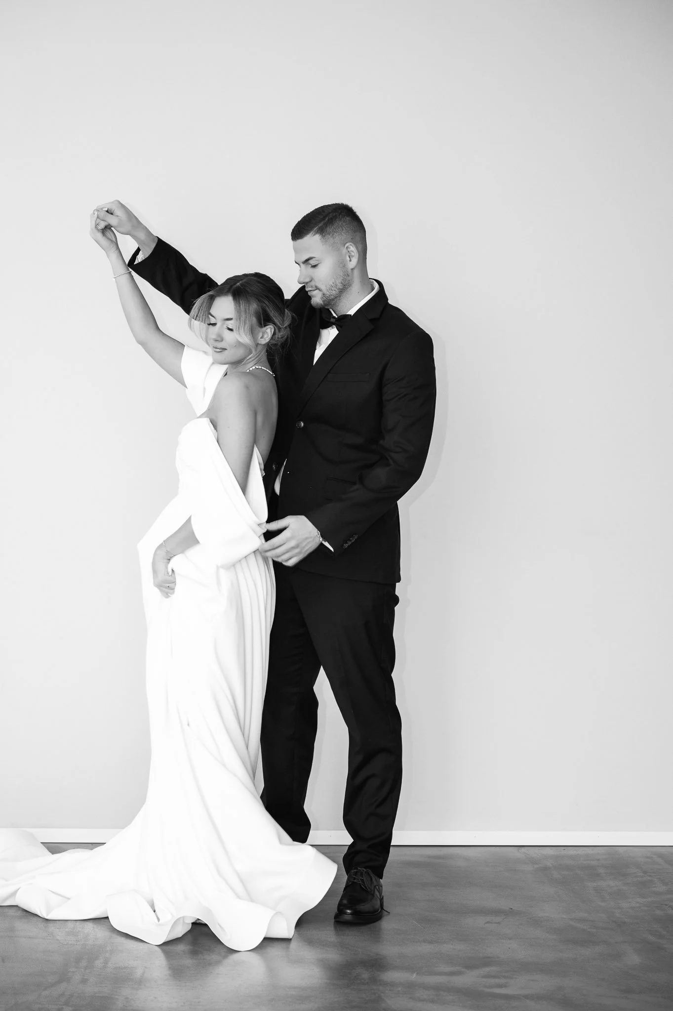 Ein schwarz-weiß Foto eines Paares bei ihrer Hochzeit, die Frau trägt ein langes weißes Hochzeitskleid und der Mann einen schwarzen Anzug mit Fliege.