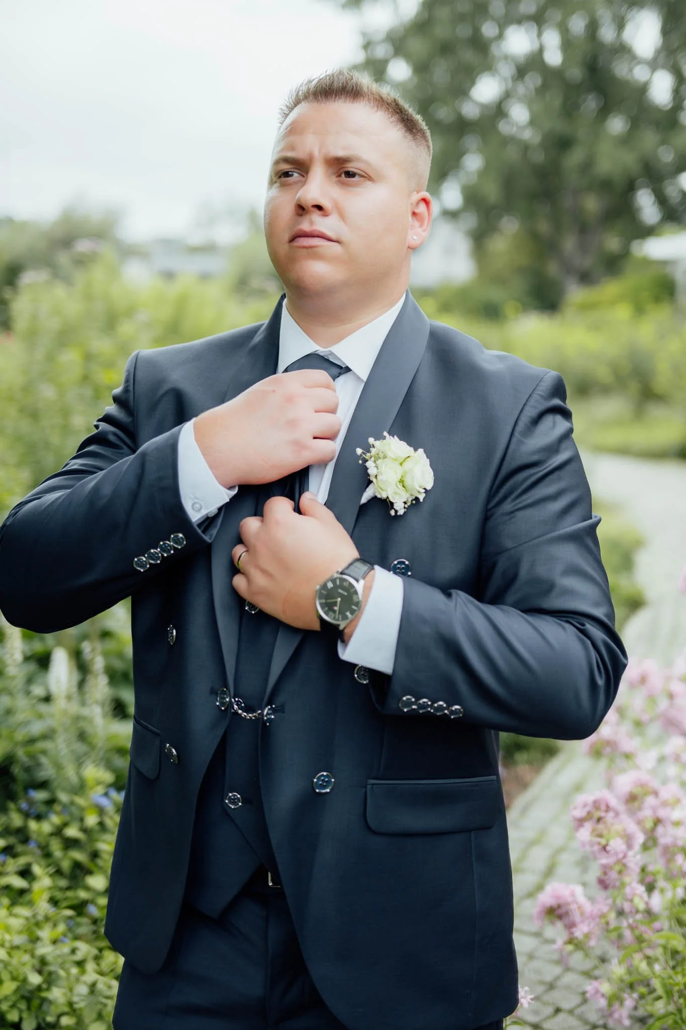 Junger Mann in Anzug passt seine Krawatte an bei einem formellen Anlass im Freien.