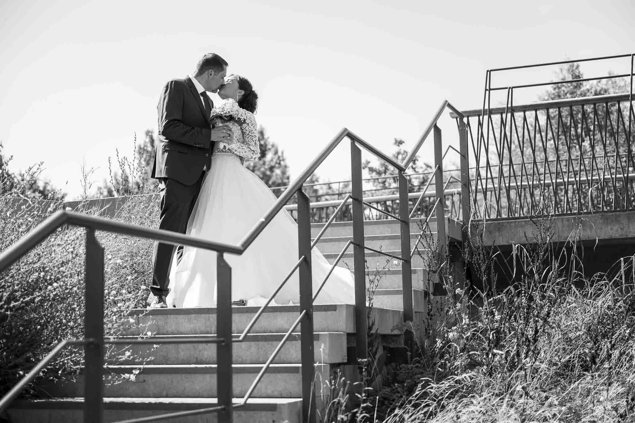 Schwarzweiß Bild von einem Brautpaar, das sich auf einer Treppe küsst