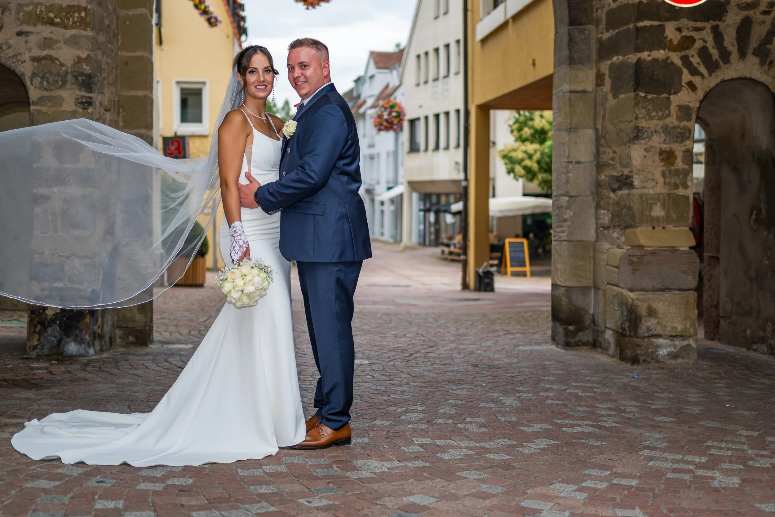 Ein Brautpaar lächelt glücklich in die Kamera in einer Altstadt