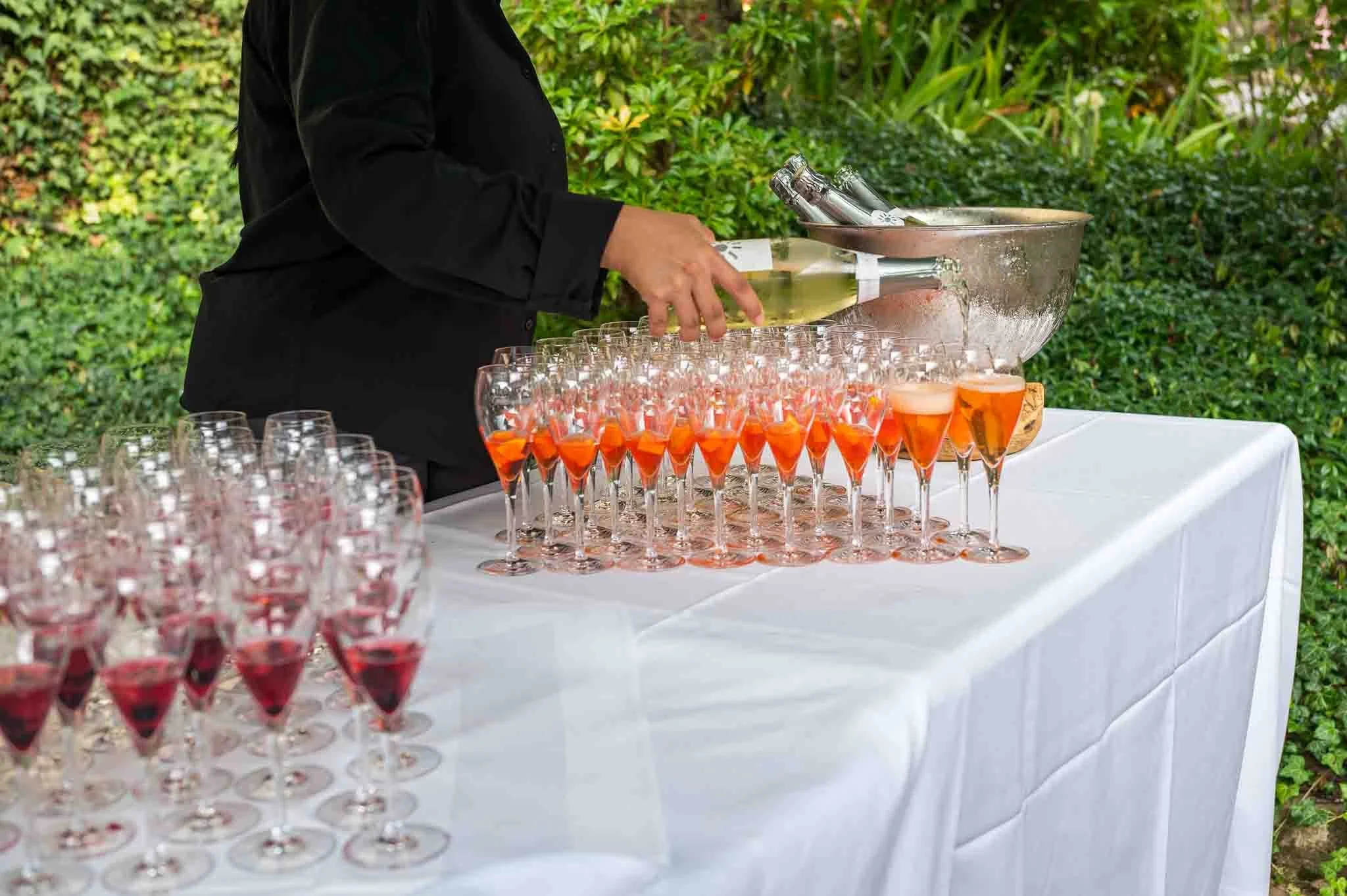 Aufnahme von einem Tisch, der mit halbtollen Sektgläsern gedeckt ist, die gerade aufgefüllt werden