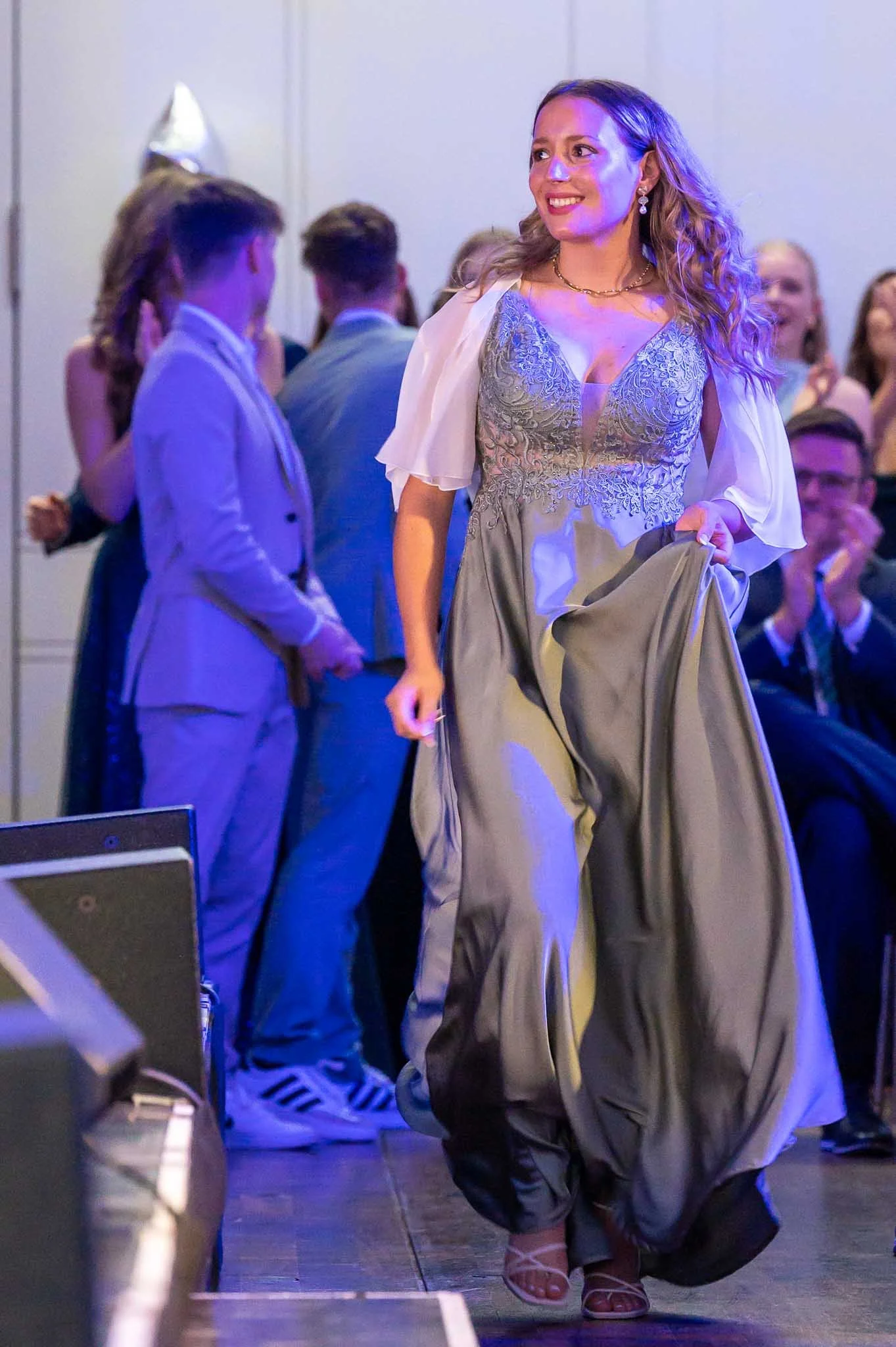 Eine Absolventin in einem eleganten langen Kleid schreitet stolz auf die Bühne beim Abiball entlang