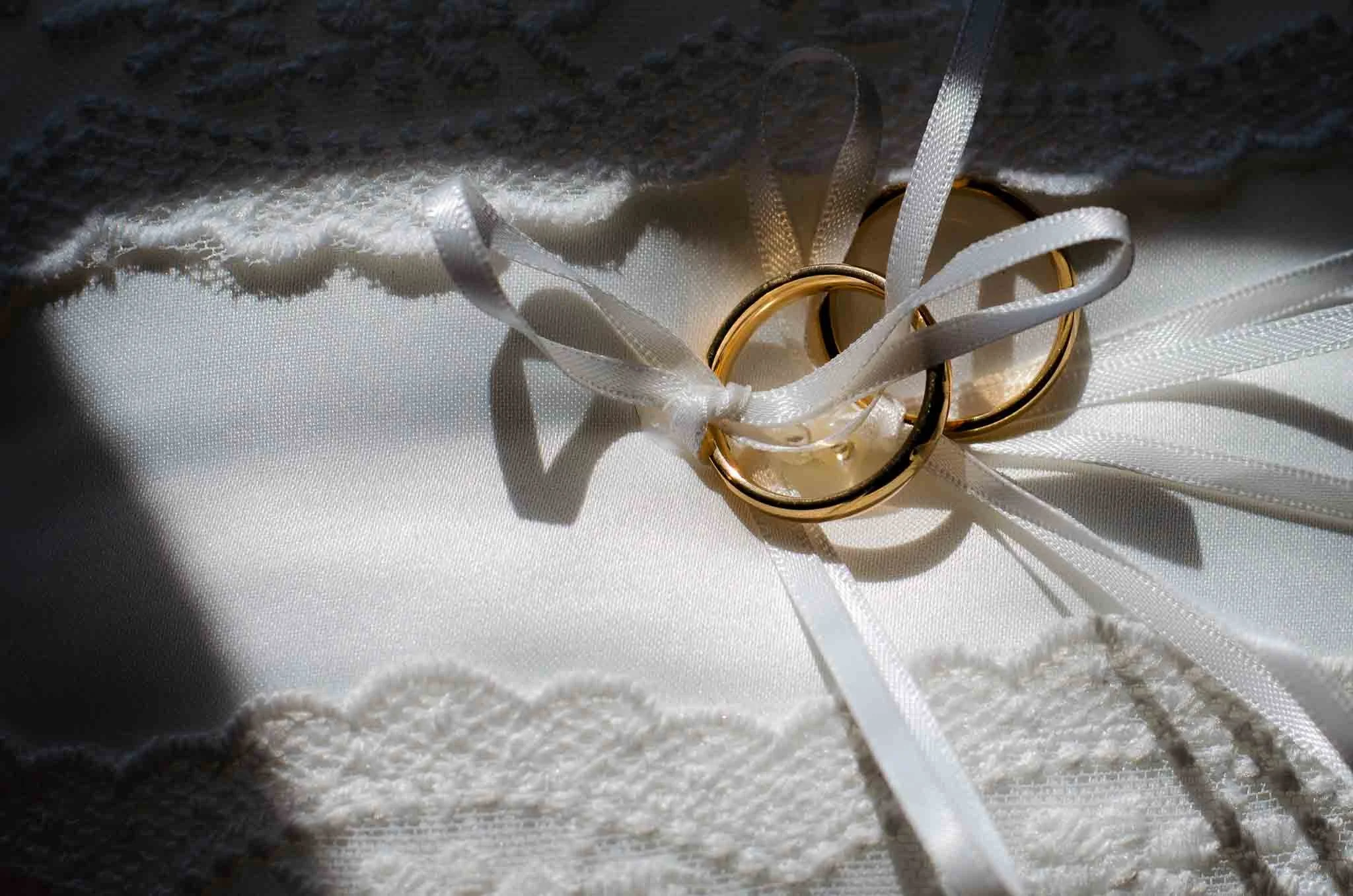 Zwei goldene Eheringe liegen auf einem weißen Satin-Kissen, das mit Spitze verziert ist.