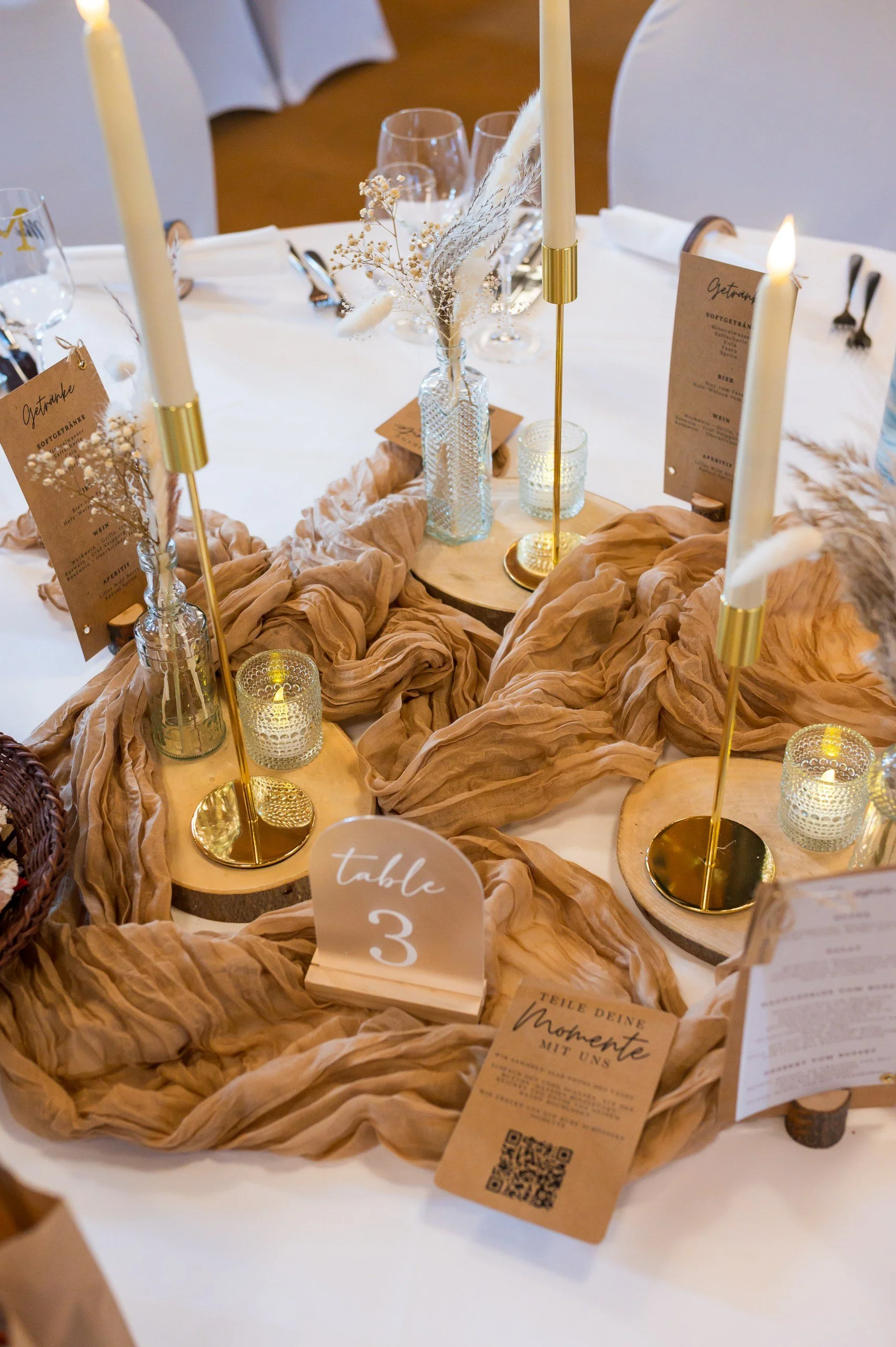 Tischdekoration bestehend aus braunen Tüchern, goldenen Kerzenhaltern, gläsernen Teelichthaltern, Trockenblumen und brauner Papeterie aus Kraftpapier