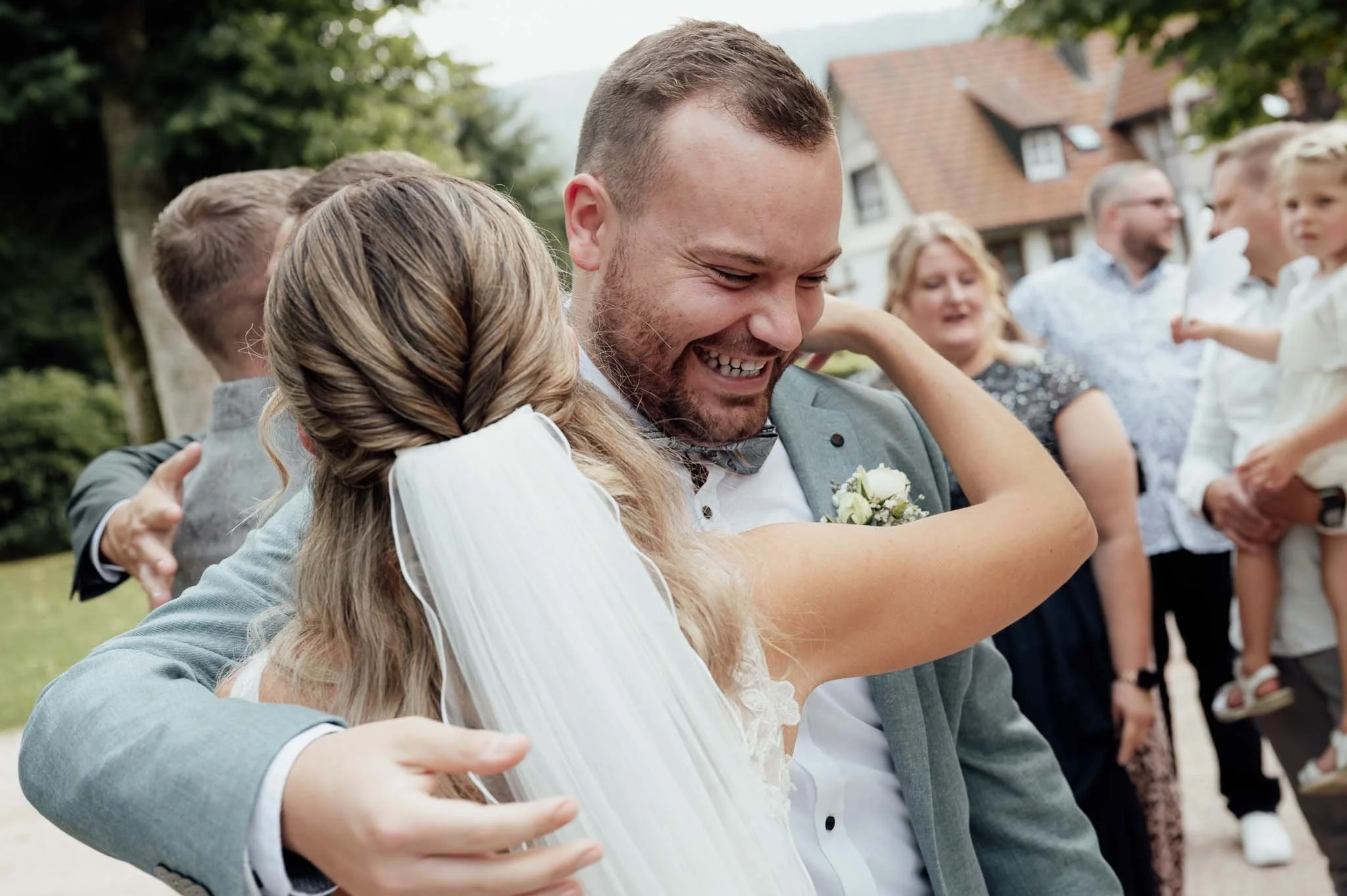 Hochzeitspaar tanzt umarmt im Freien, lachend, umgeben von Gästen.