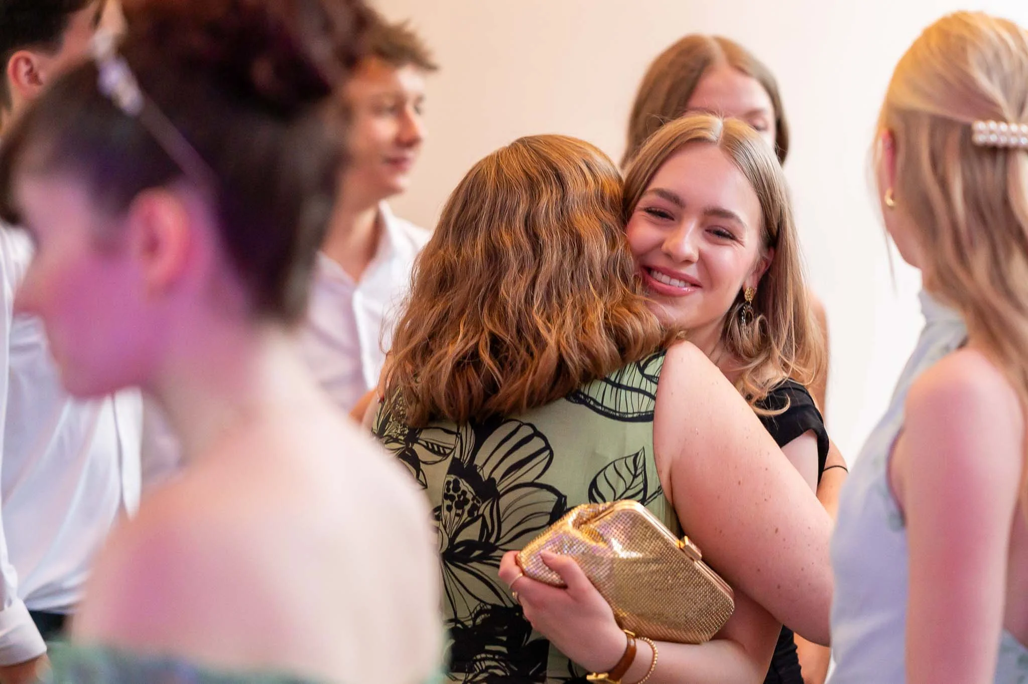 Auf dem Abiball umarmen sich zwei Frauen herzlich inmitten von Schülern und LehrernAuf dem Abiball umarmen sich zwei Frauen herzlich inmitten von Schülern und Lehrern