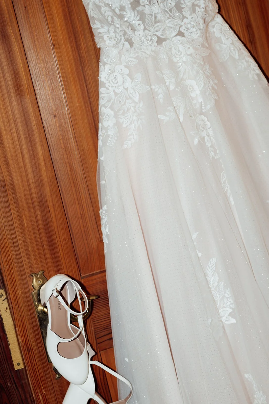 Künstlerisches Bild eines Hochzeitskleides, welches an einer Türk hängt. An der Türklinke hängen die Brautschuhe