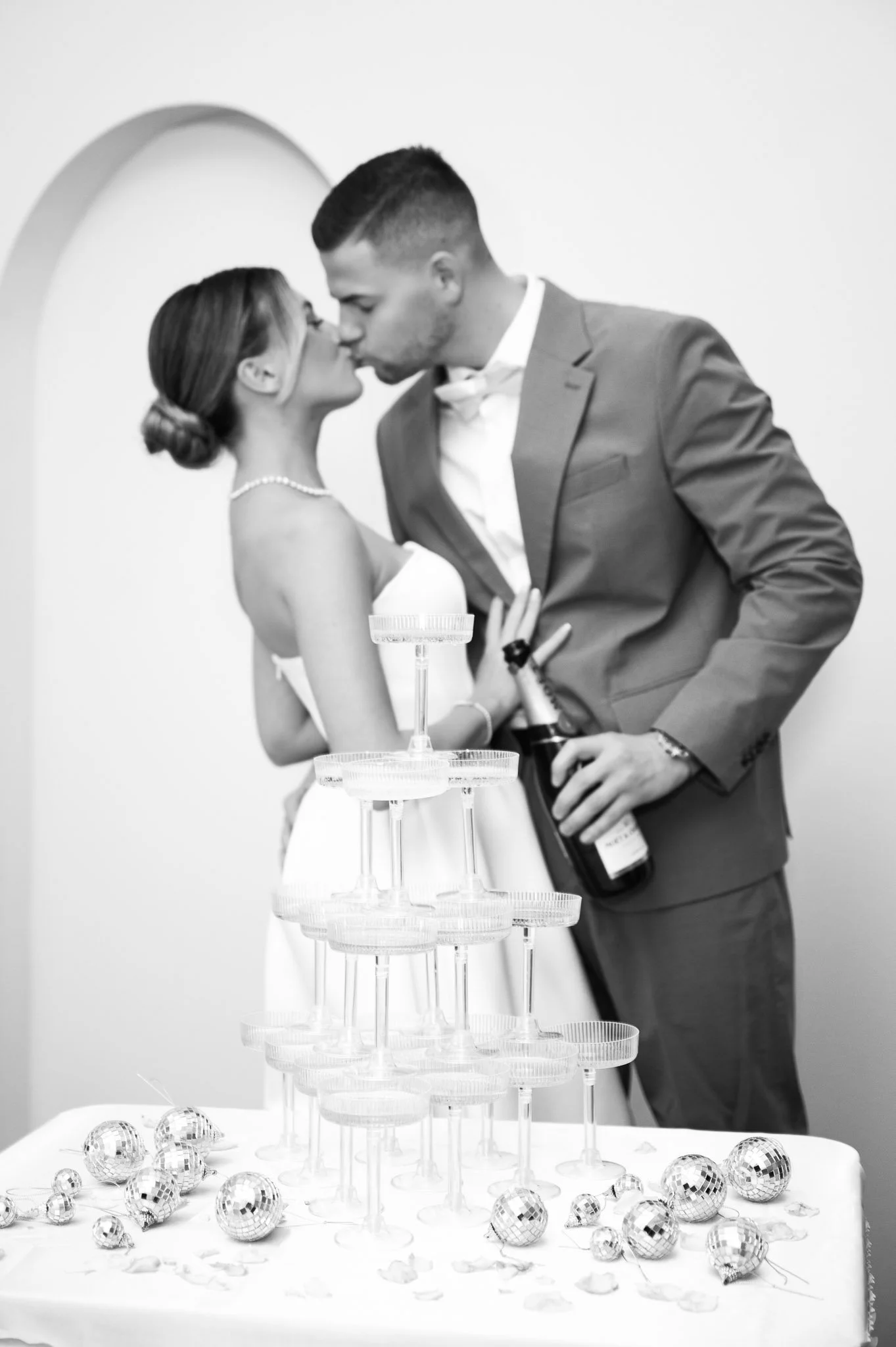 Braut und Bräutigam küssen sich bei ihrer Hochzeit, Silvester-Party mit Sekt und Dekorationen im Hintergrund, schwarz-weiß Fotografien.