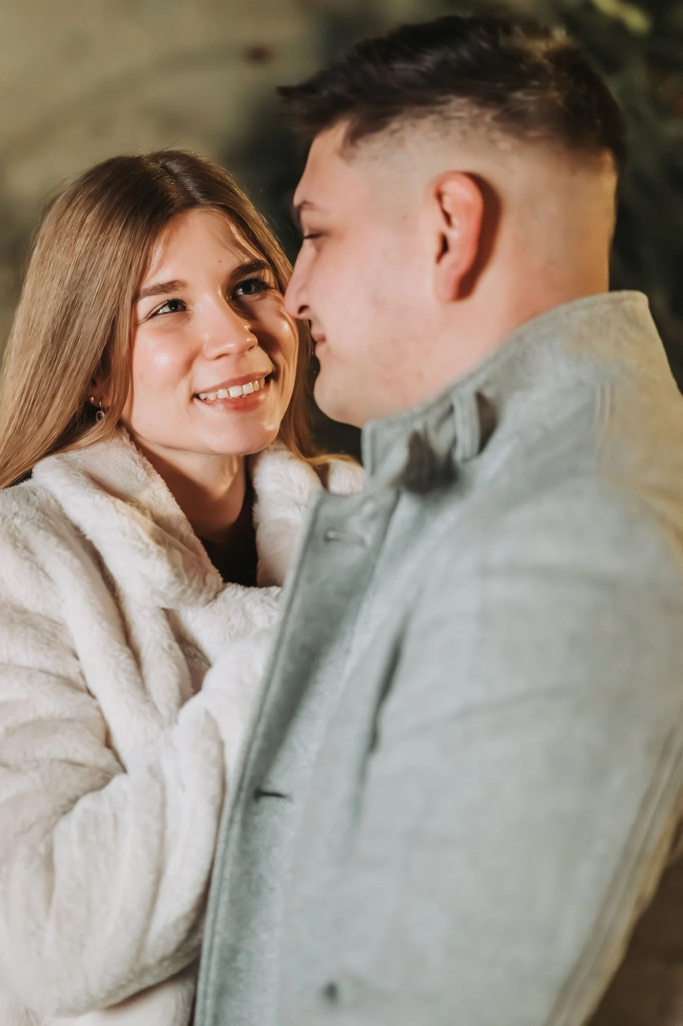 Nahaufnahme einer Frau, die einen Mann, der direkt vor ihr steht, verliebt ansieht. Beide tragen schicke  Wintermantel.