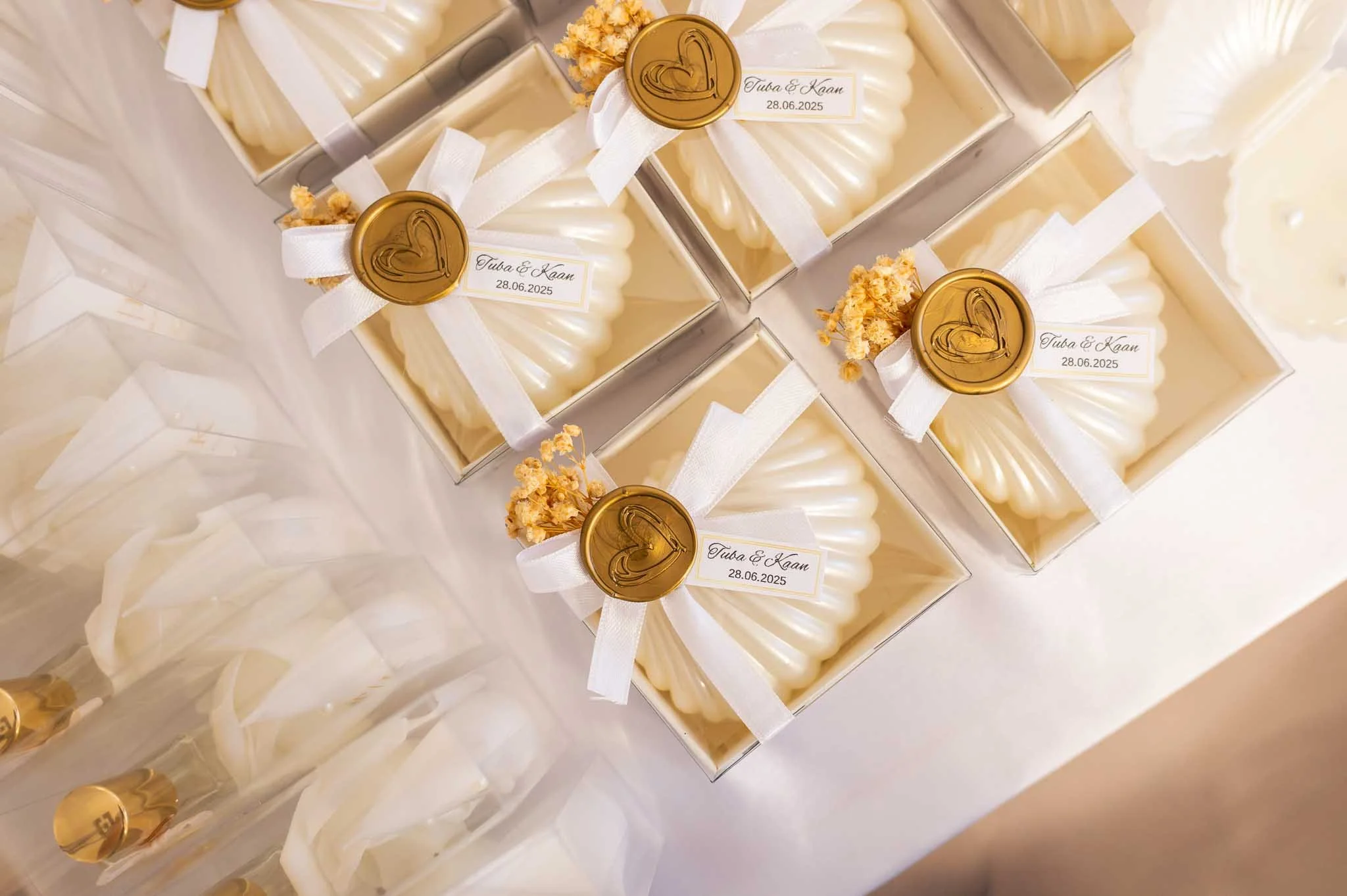Geschenke in weißem Geschenkpapier mit weißen Bändern, gekrönt mit goldenen Siegeln, die Herz und Namen sowie das Datum 28.06.2025 tragen.