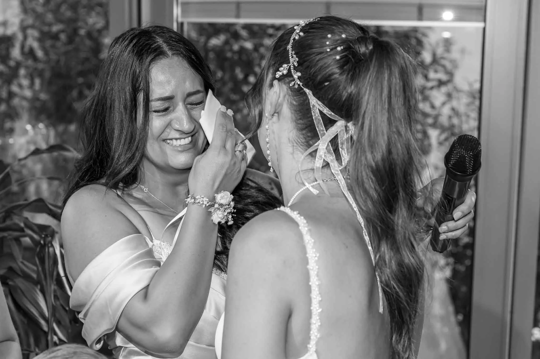 Zwei Frauen bei einer emotionalen Szene, eine weint und hält ein Taschentuch, die andere hält ein Mikrofon, beide tragen elegante Kleider und Schmuck.
