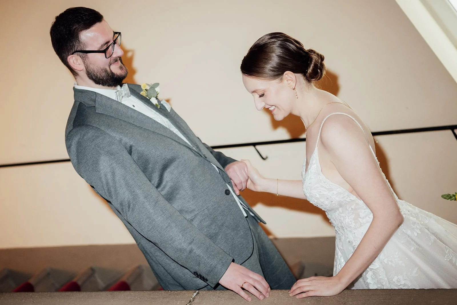 Bild von einem Brautpaar, was gerade auf einer Treppe steht. Beide blicken lachend zu Boden