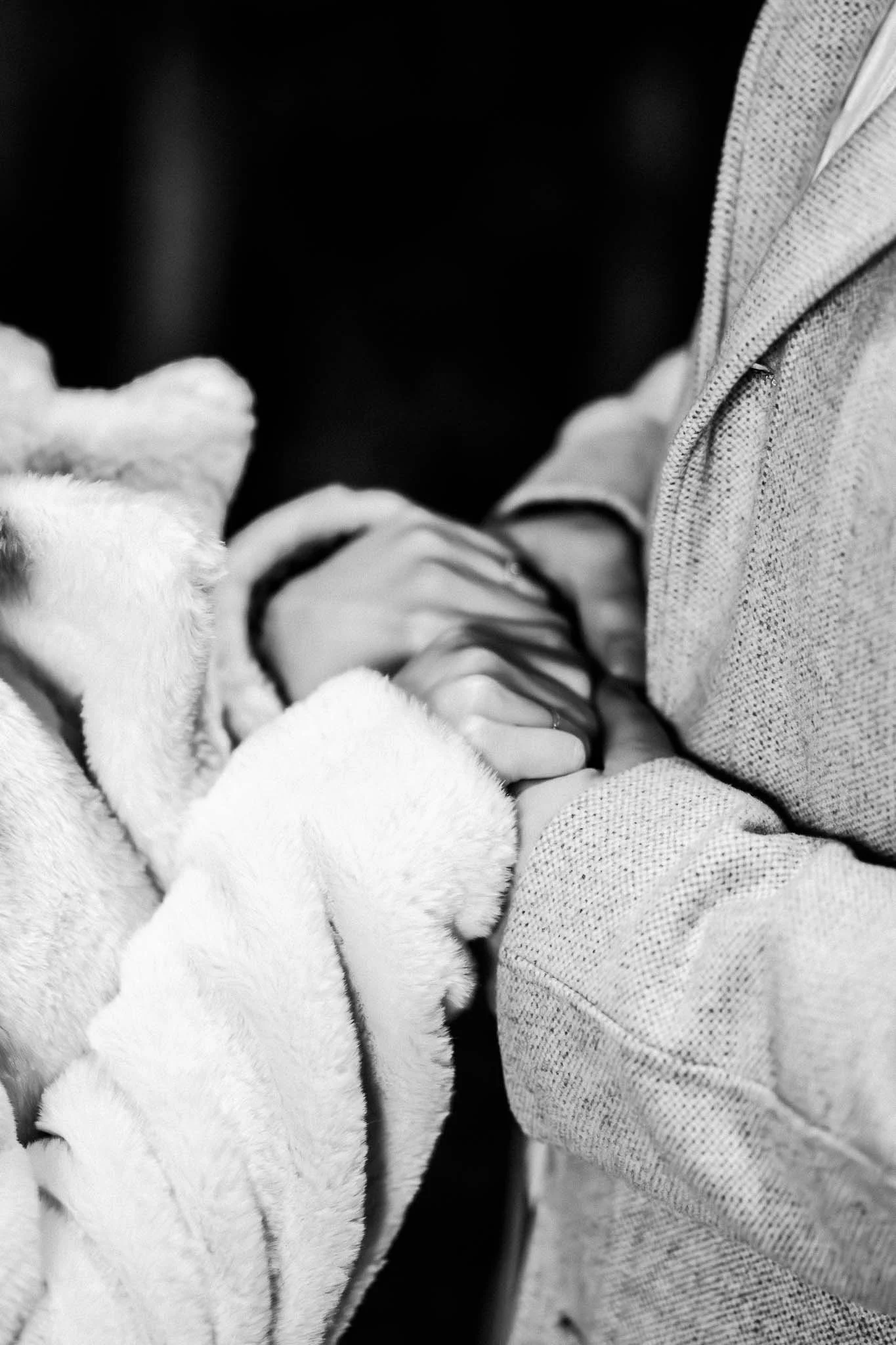 Nahaufnahme von einem Mann und einer Frau, wie er mit beiden Händen ihre beiden Hände hält. Sie tragen Mäntel und das Bild ist in Schwarz-weiß