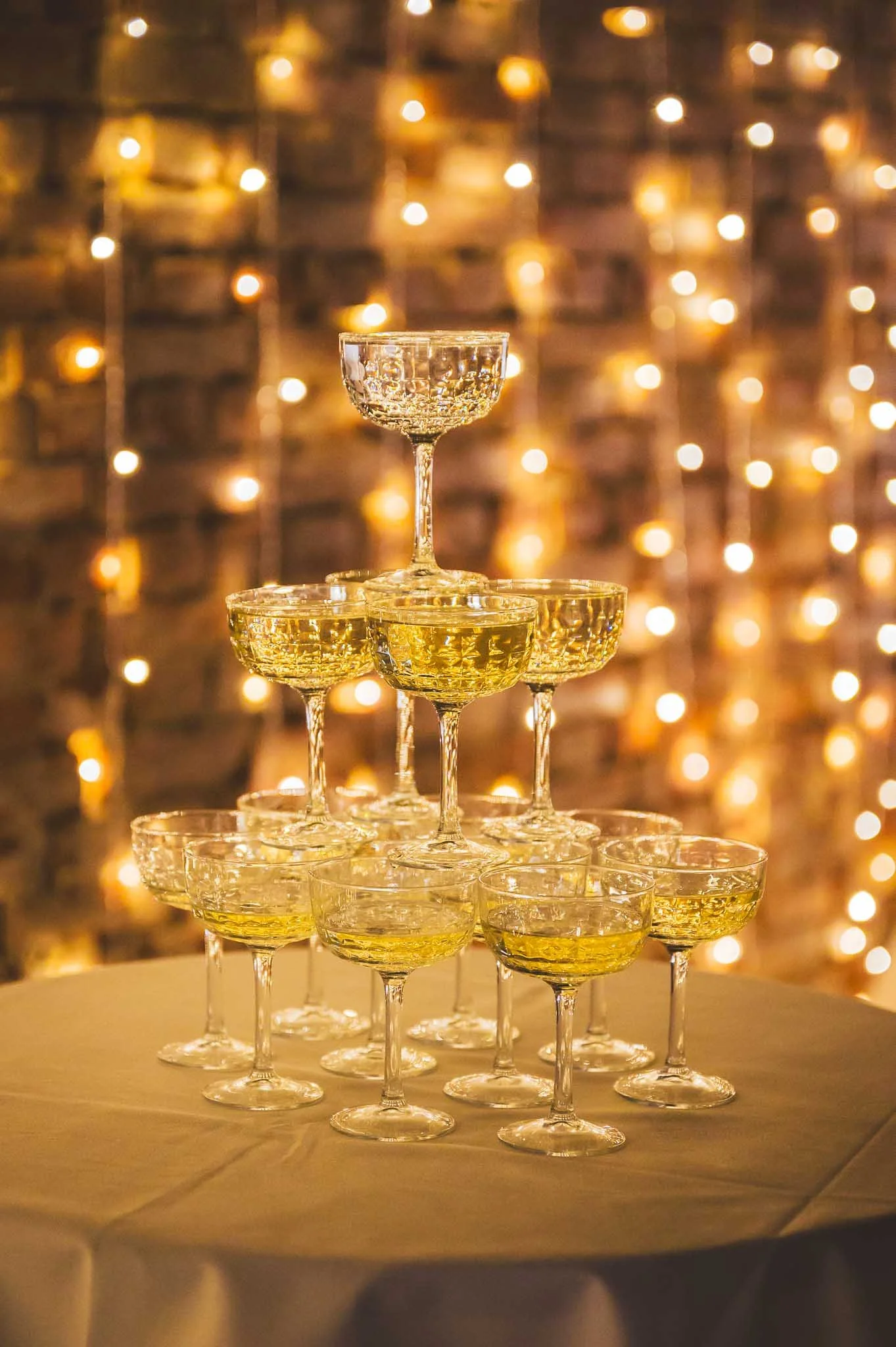 Ein Champagner-Tower aus Gläsern auf einem Tisch, im Hintergrund bunte Lichter.