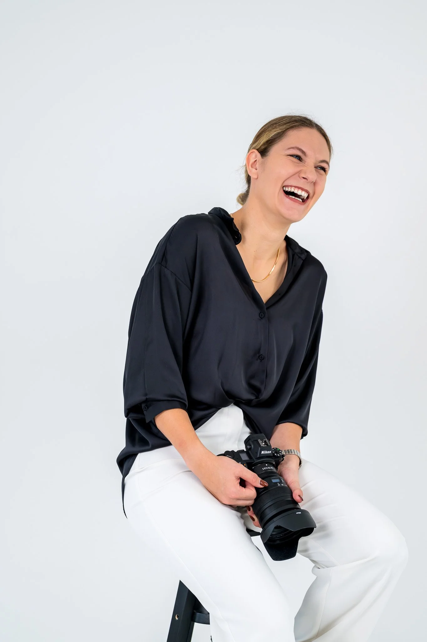 Eine Frau lacht während sie auf einem Barhocker sitzt und eine Kamera in ihrem Schoß hält