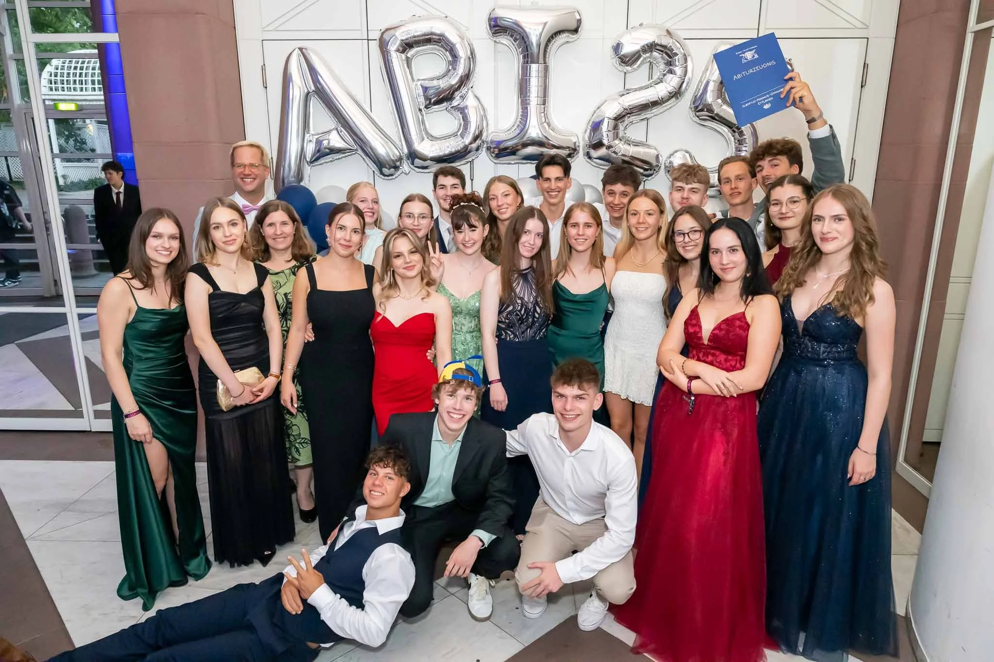 Eine Gruppe von Menschen posiert fröhlich vor einem großen Abiball-Schild für ein Foto