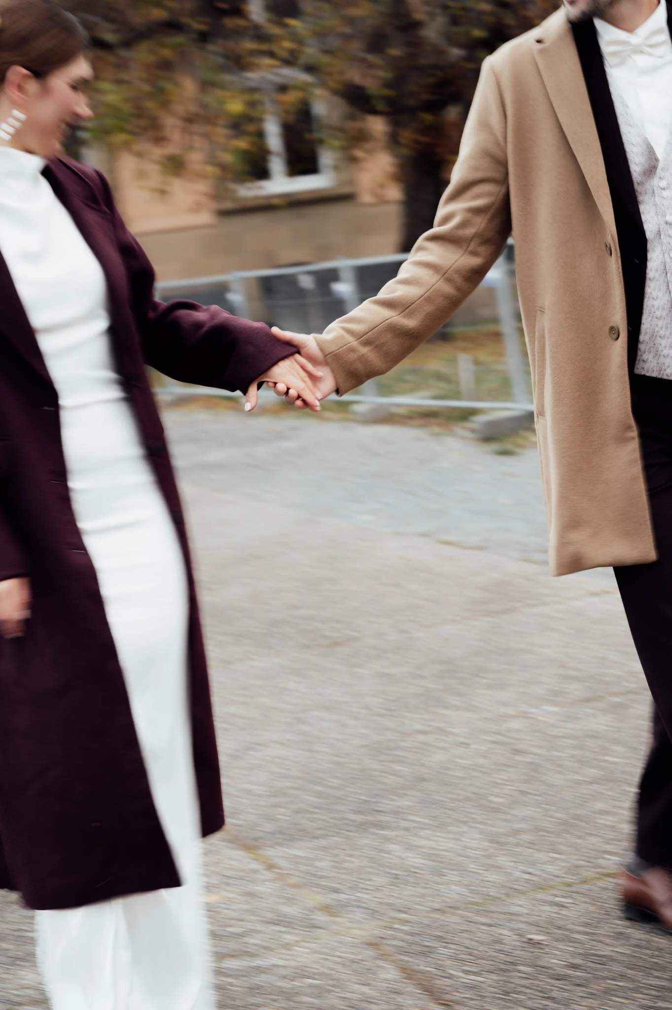 Zwei Menschen halten Händchen, während sie spazieren gehen, draußen mit herbstlichen Bäumen im Hintergrund.