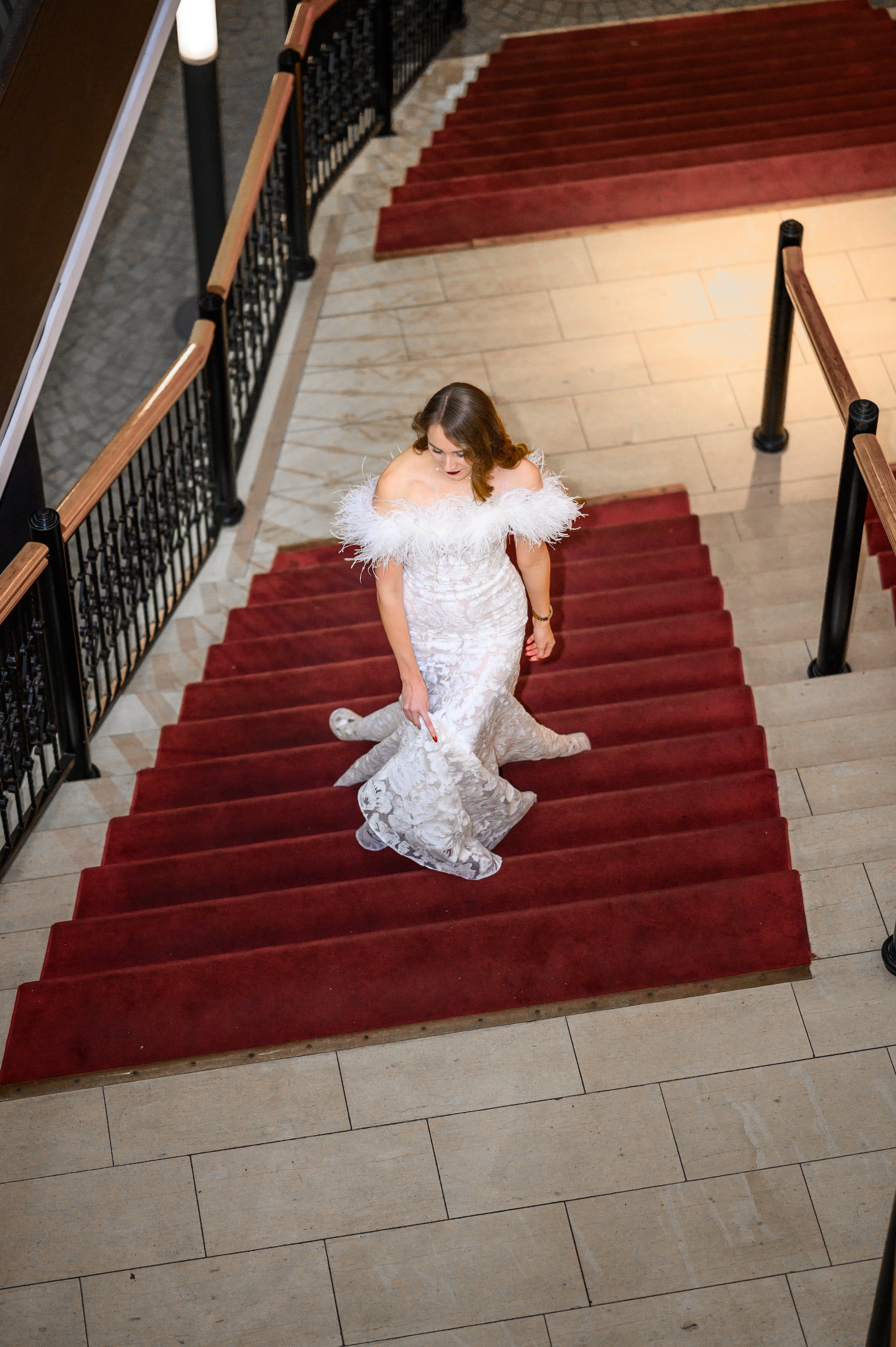 Bild aus der Vogelperspektive auf eine Braut, die eine Treppe mit rotem Teppich hoch läuft.