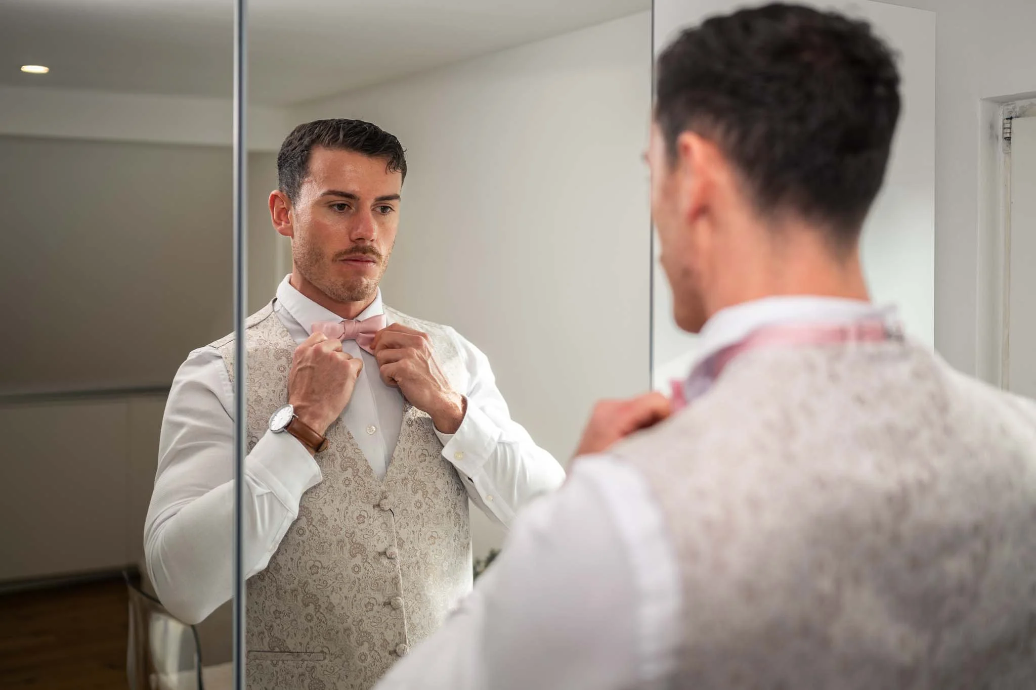 Ein Bild von einem Mann, der sich im Spiegel die Fliege seines Anzugs richtet