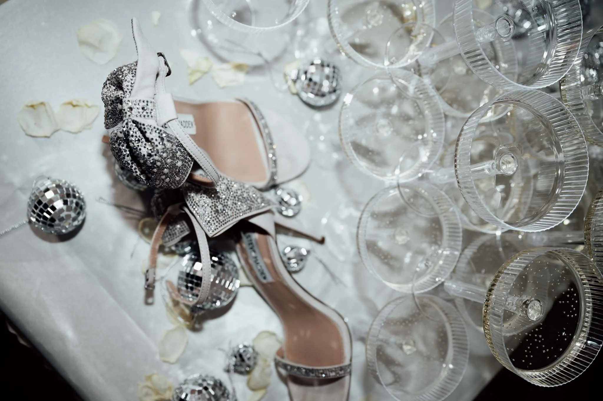 Silberne Schmuckstücke, leere Gläser und weisse Rosenblätter auf einem Tisch, stilvolle Anordnung für eine Feier oder Party.