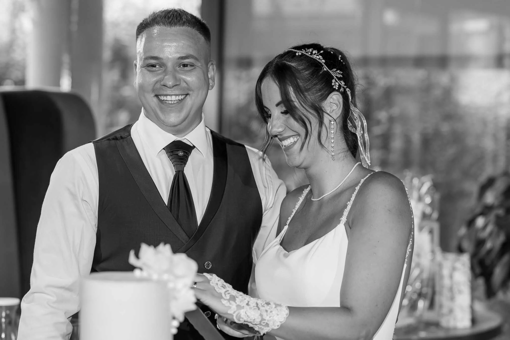 Ein glückliches Paar bei einer Hochzeit, lachend, mit einem Hochzeitstorte im Vordergrund.