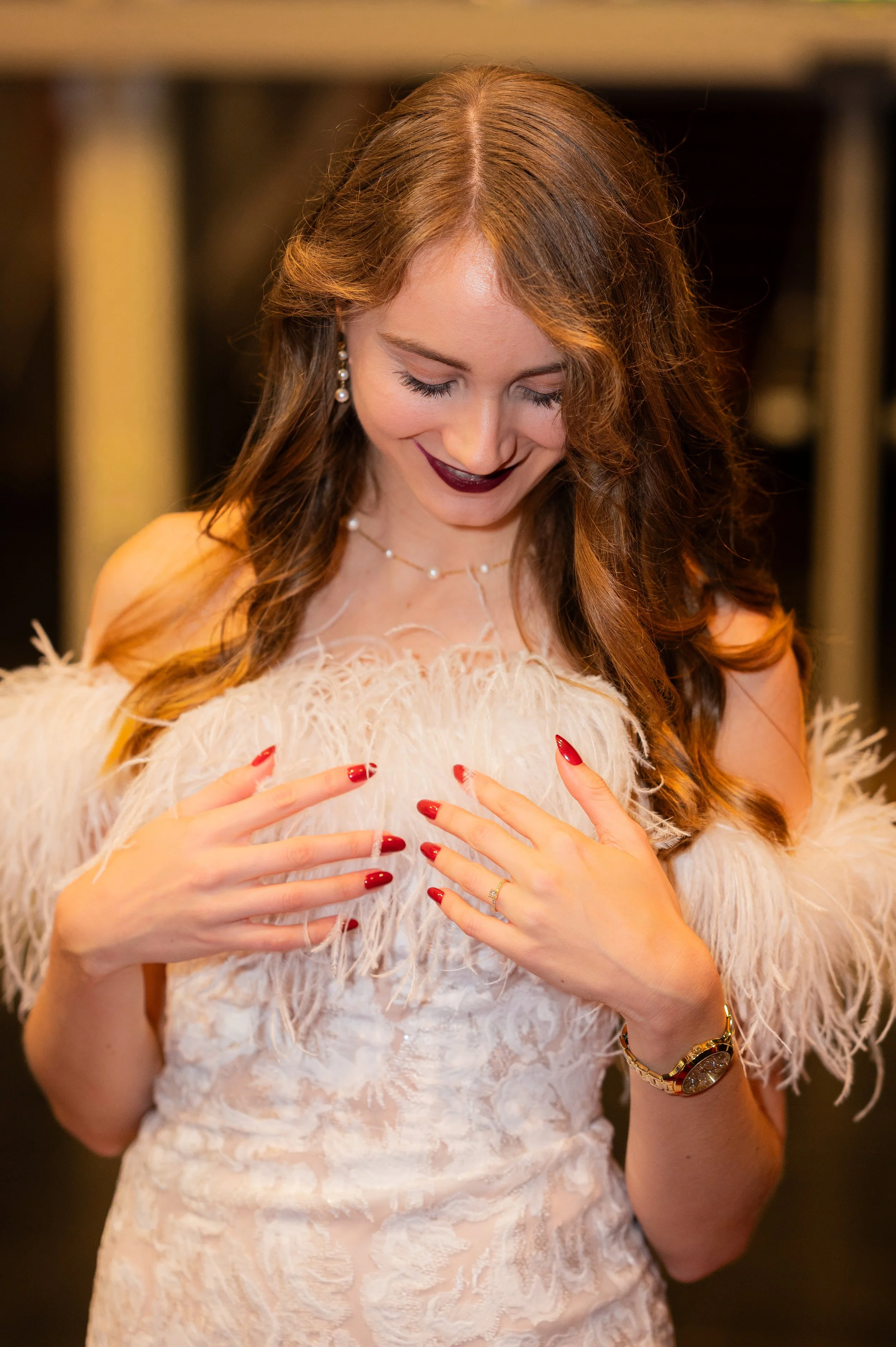 Porträt einer Braut, die lachend auf ihre Hände blickt, die sie auf ihrer Brust abgelegt hat. Die Stimmung ist warm und herzlich