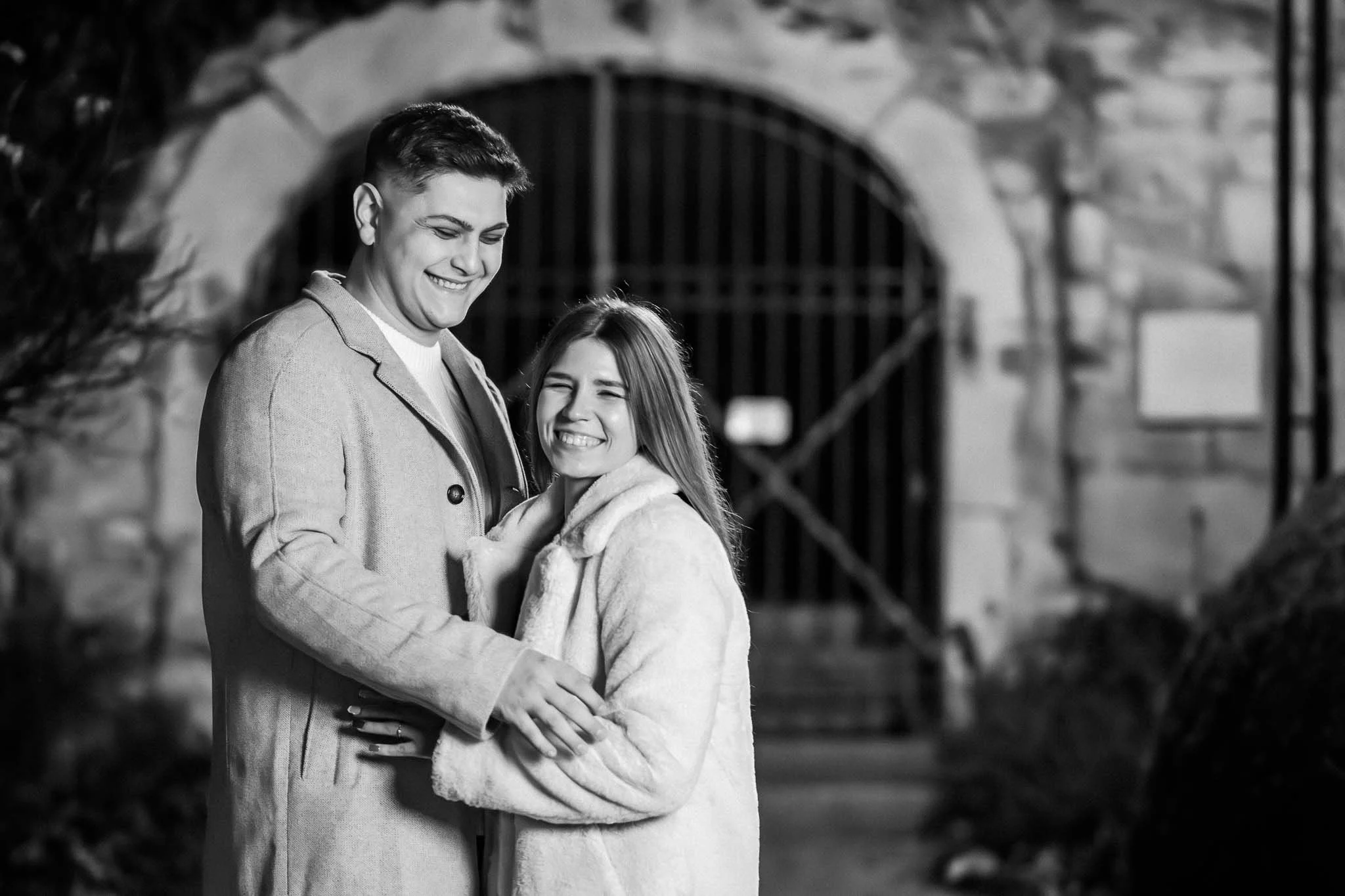 Schwarz-weiß Halbkörper Portrait vn einem Mann und einer Frau, die in einer leichten Umarmung herzlich lachen.