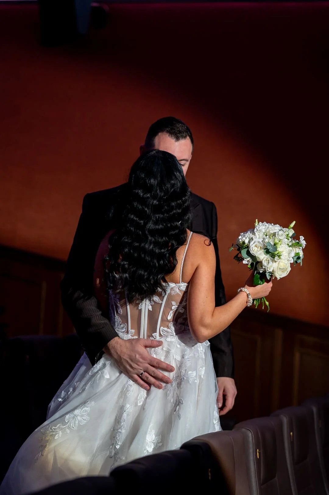 Aufnahme eines Brautpaares von hinten, wie sie sich im Spotlight eines Kinosaals küssen