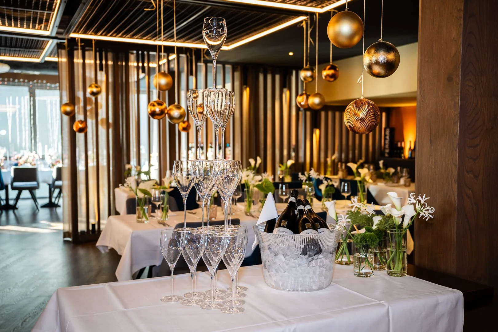 Ein Turm aus Sektgläsern auf einem Tisch mit einem Kübel Sektflaschen und Blumen in einem stilvollen Restaurant