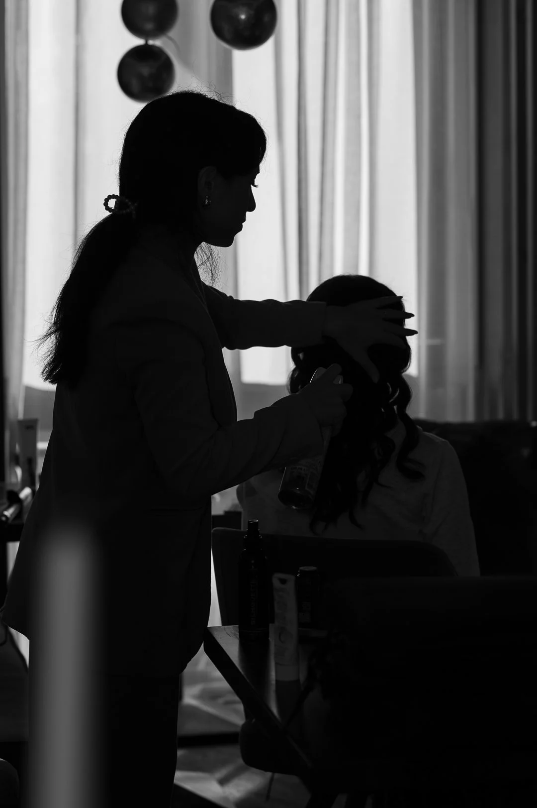 Schwarzweiß Bild von einer Frau, die einer anderen die Haare macht. Es sind nur Silhouetten zu erkennen