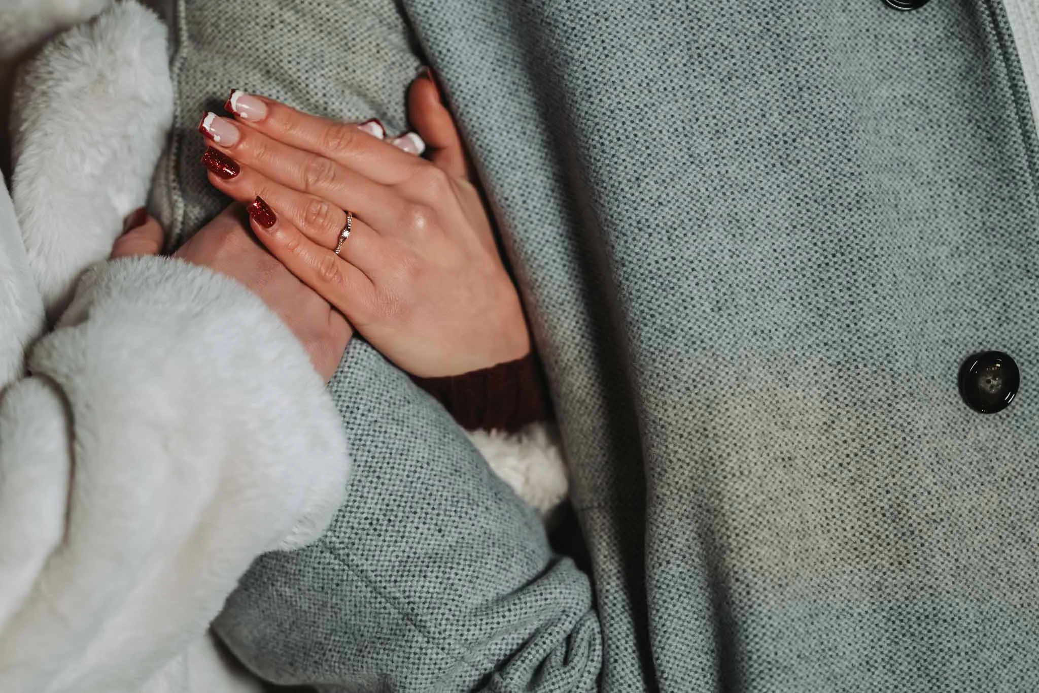 Die Hände einer Frau umschlingen den Oberarm einer Person. An ihrer Hand ist ein Ring zu sehen. Beide tragen dicke Mäntel.