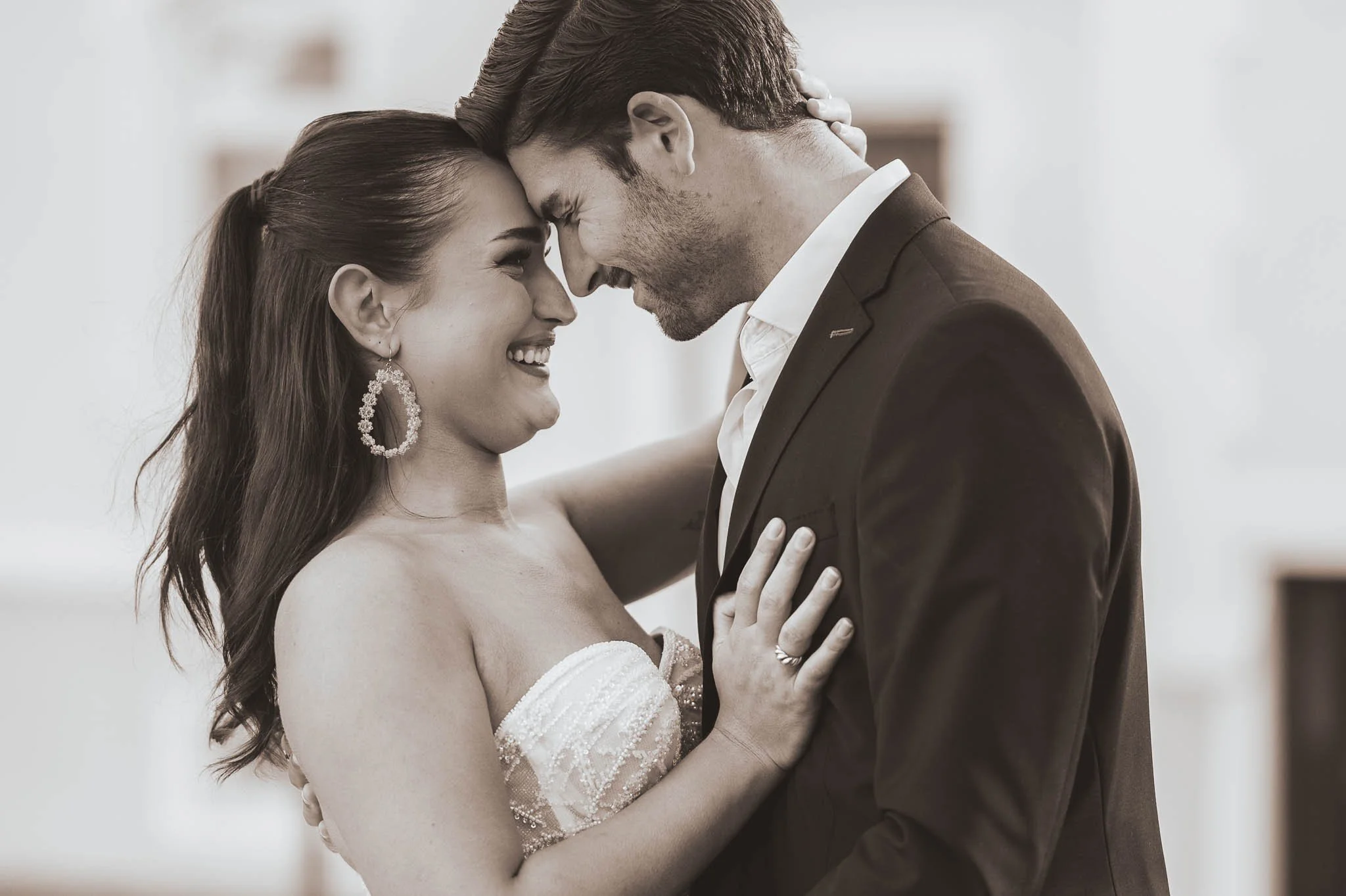 Ein glückliches Paar bei einer Hochzeit, umarmt und lächelnd, mit dem Körper eng aneinander, in einem feierlichen Umfeld.