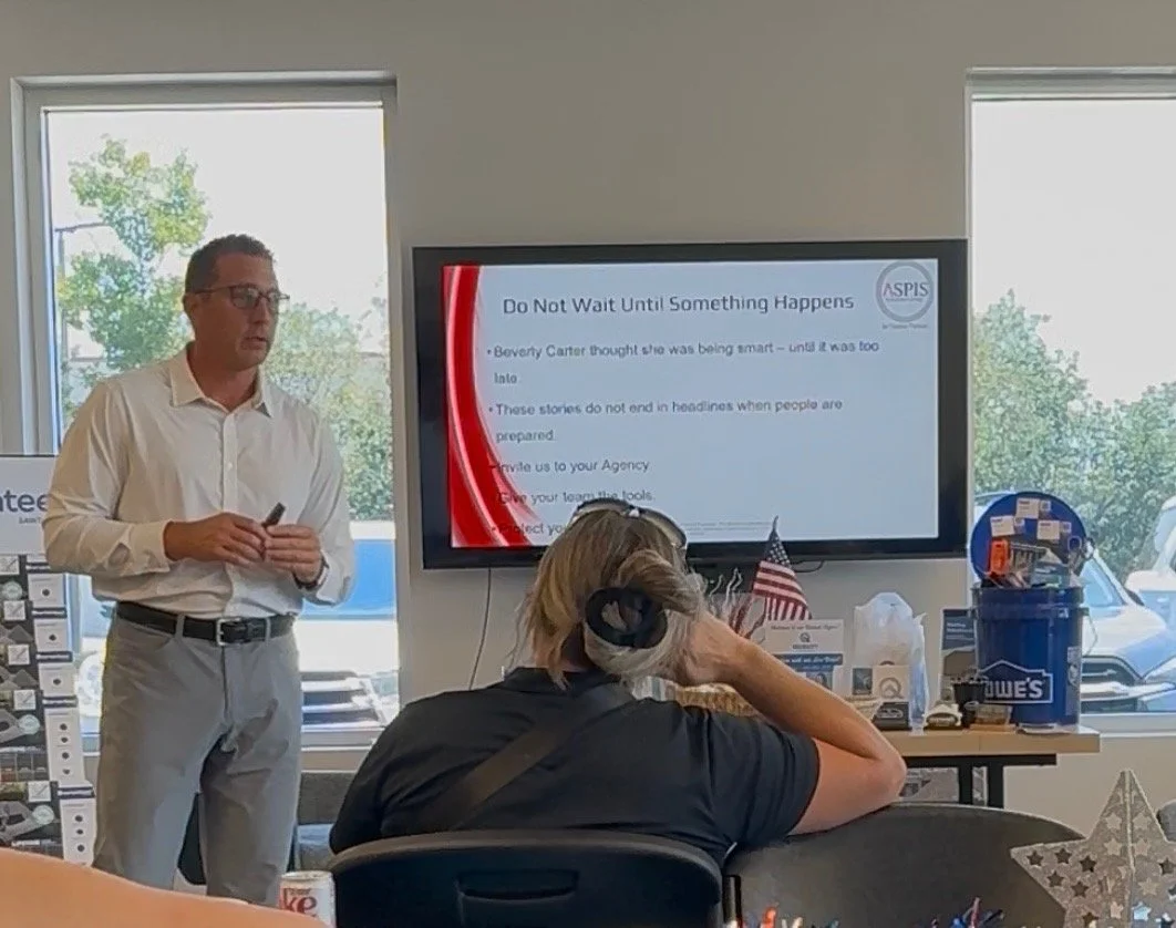 A man in glasses and a white shirt giving a presentation in a room with large windows, with a woman listening and a presentation screen displaying tips about not waiting for something to happen.