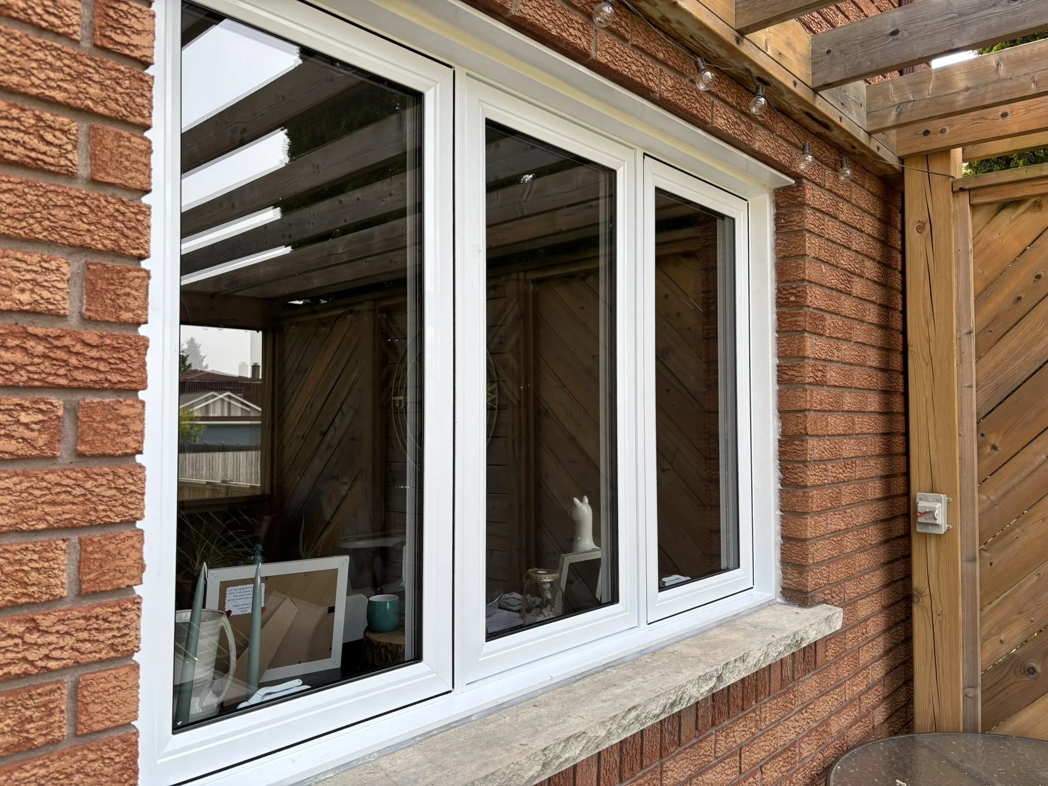 A large window with white framing in a brick wall of a house, reflecting the outside and revealing some interior decorations including a small llama figurine and framed pictures inside.