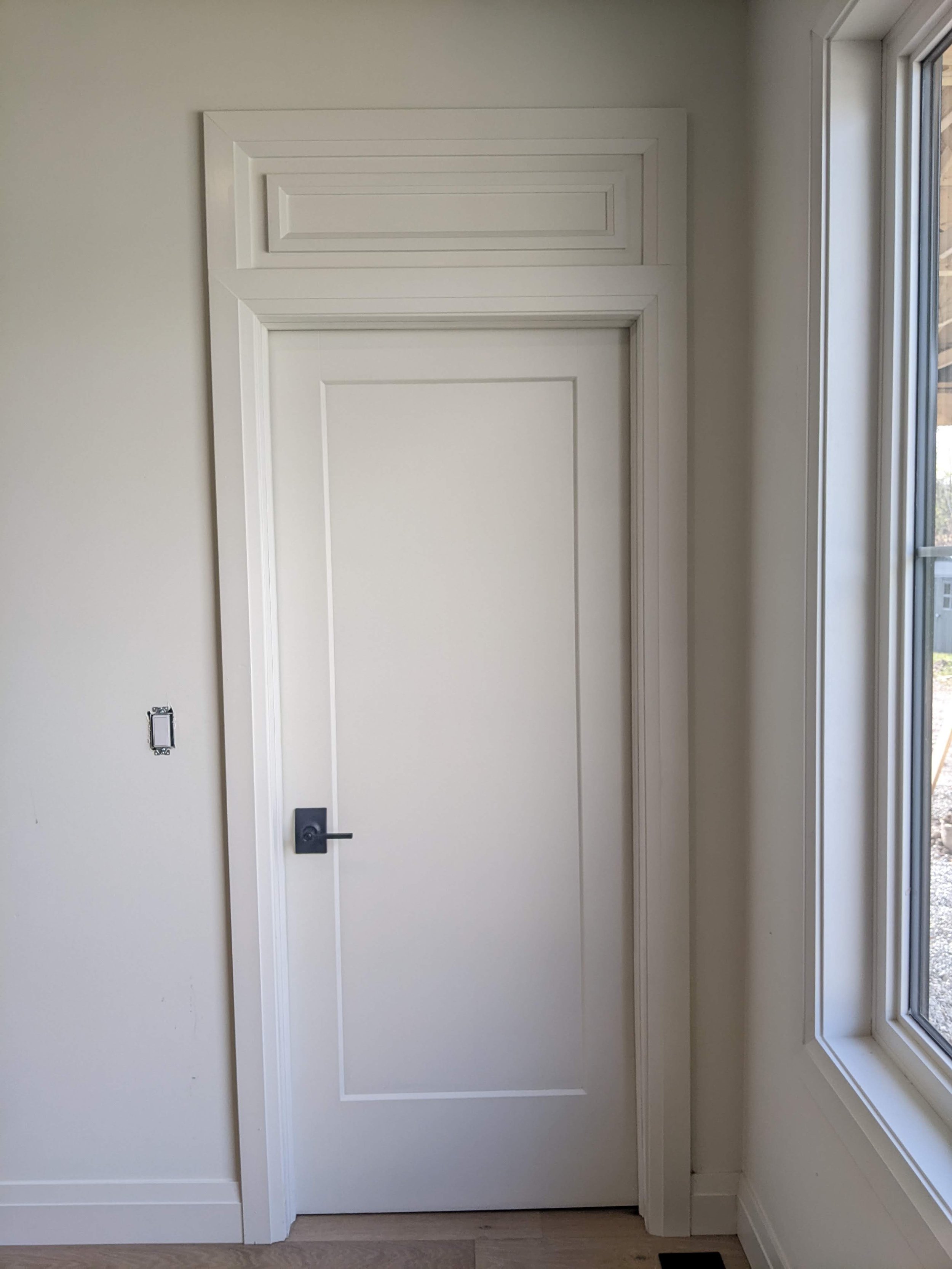 White interior door with molding, next to a window with a view of an outdoor area.