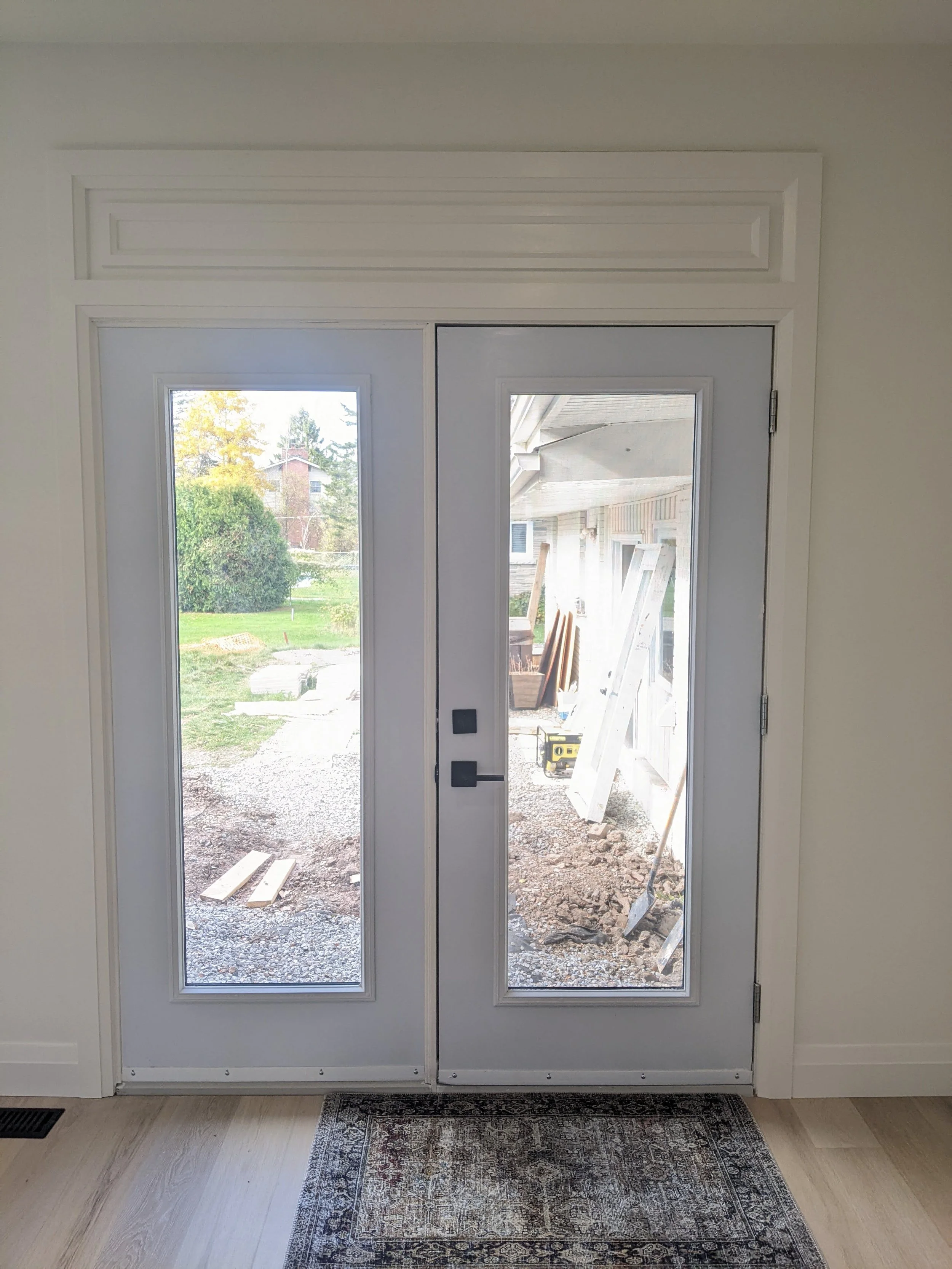 Double glass door leading to an outside construction site with dirt, tools, and building materials visible.