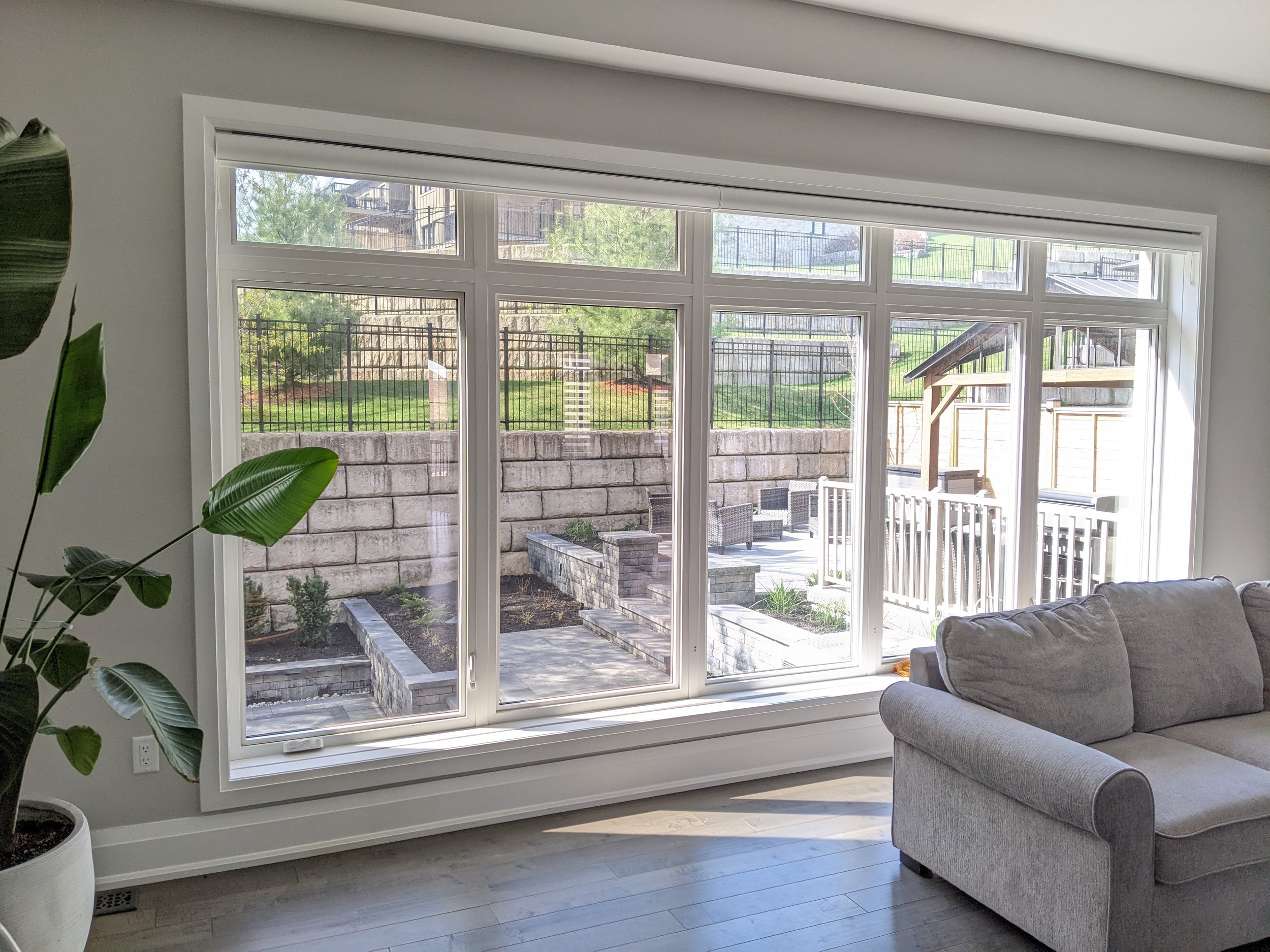 Living room with large window overlooking an outdoor patio and backyard with grass, stone walls, a fence, and outdoor furniture.