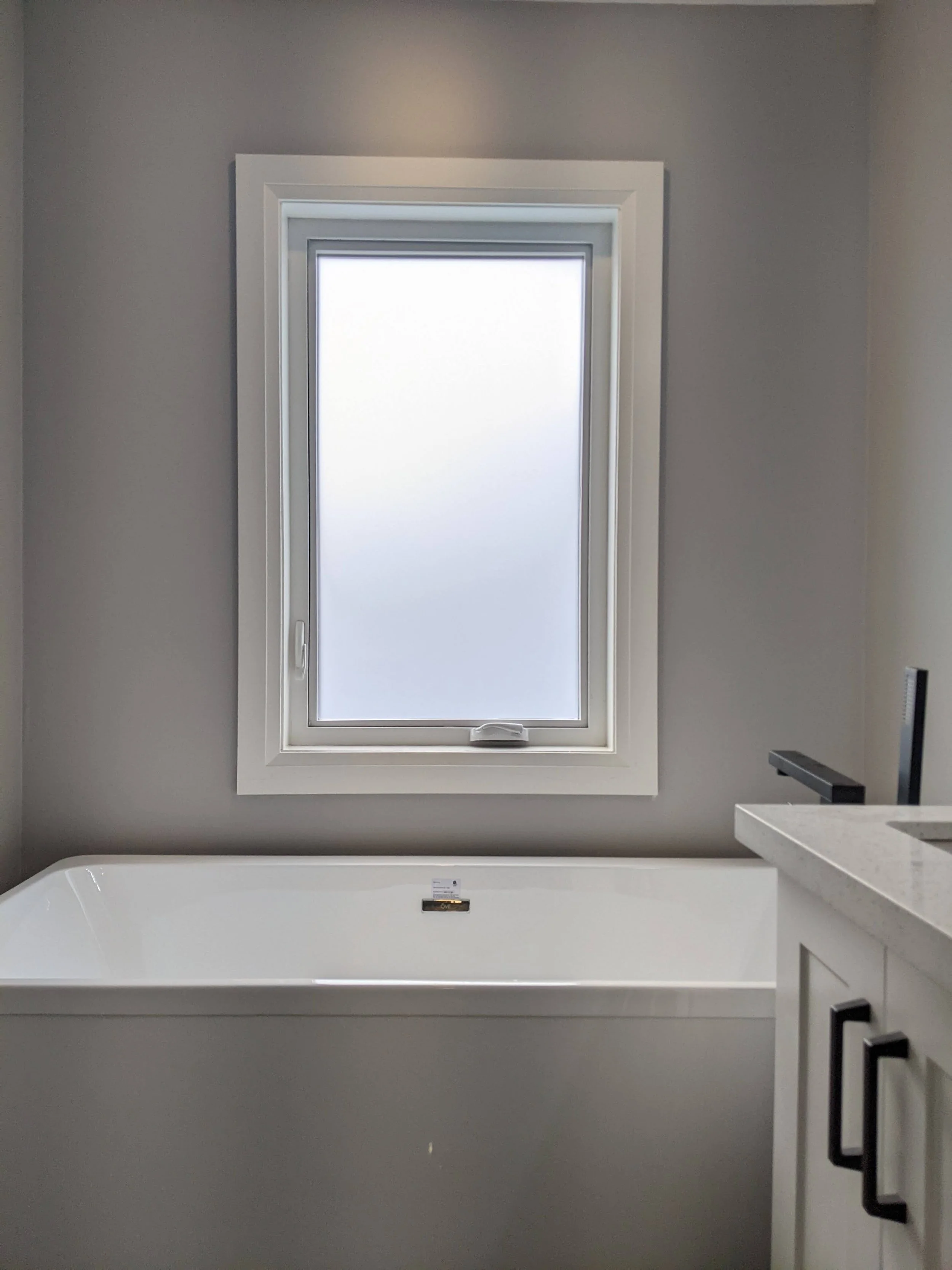 Bathroom with a bathtub under a frosted window and a white vanity with black handles on the right side.