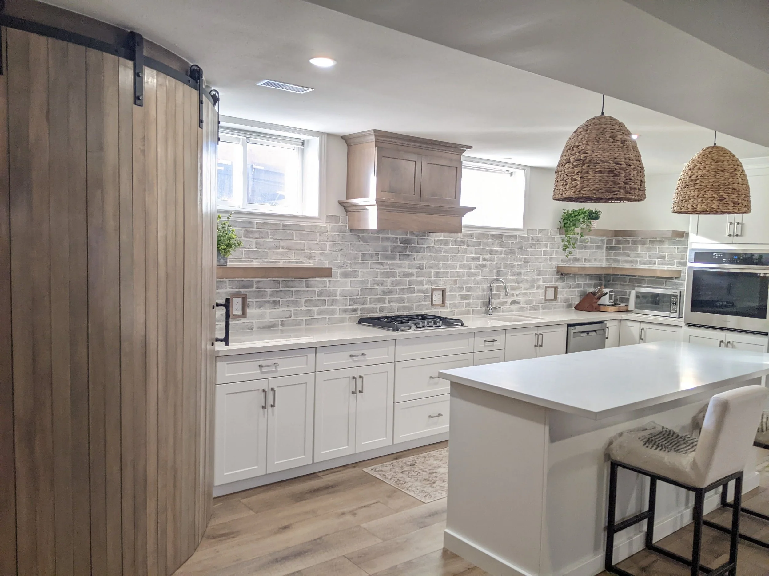 Modern farmhouse kitchen with white cabinets, brick backsplash, wooden accents, pendant lights, and kitchen appliances.