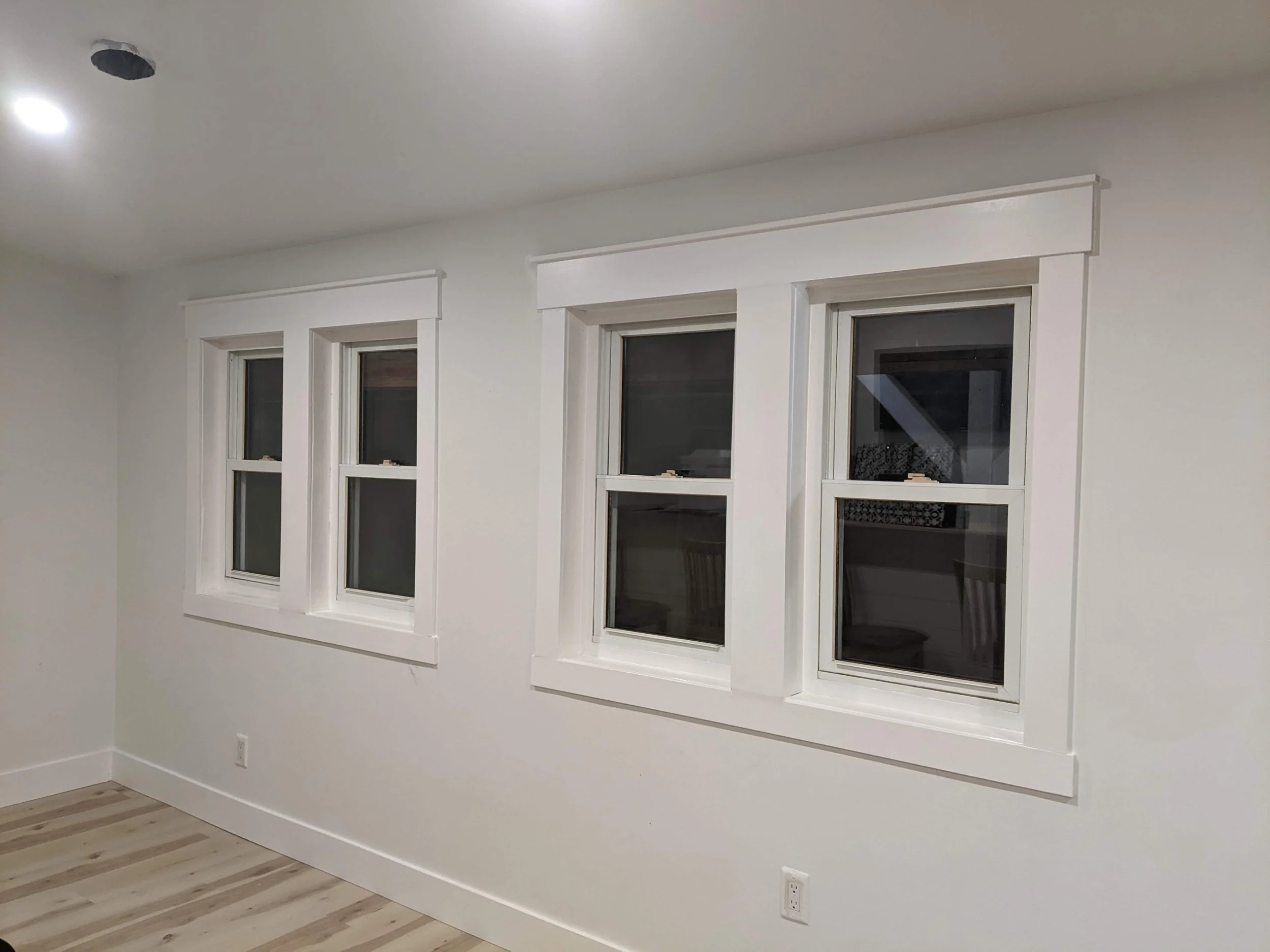 Blank white room with three double-hung windows, white trim, and light-colored hardwood floors.