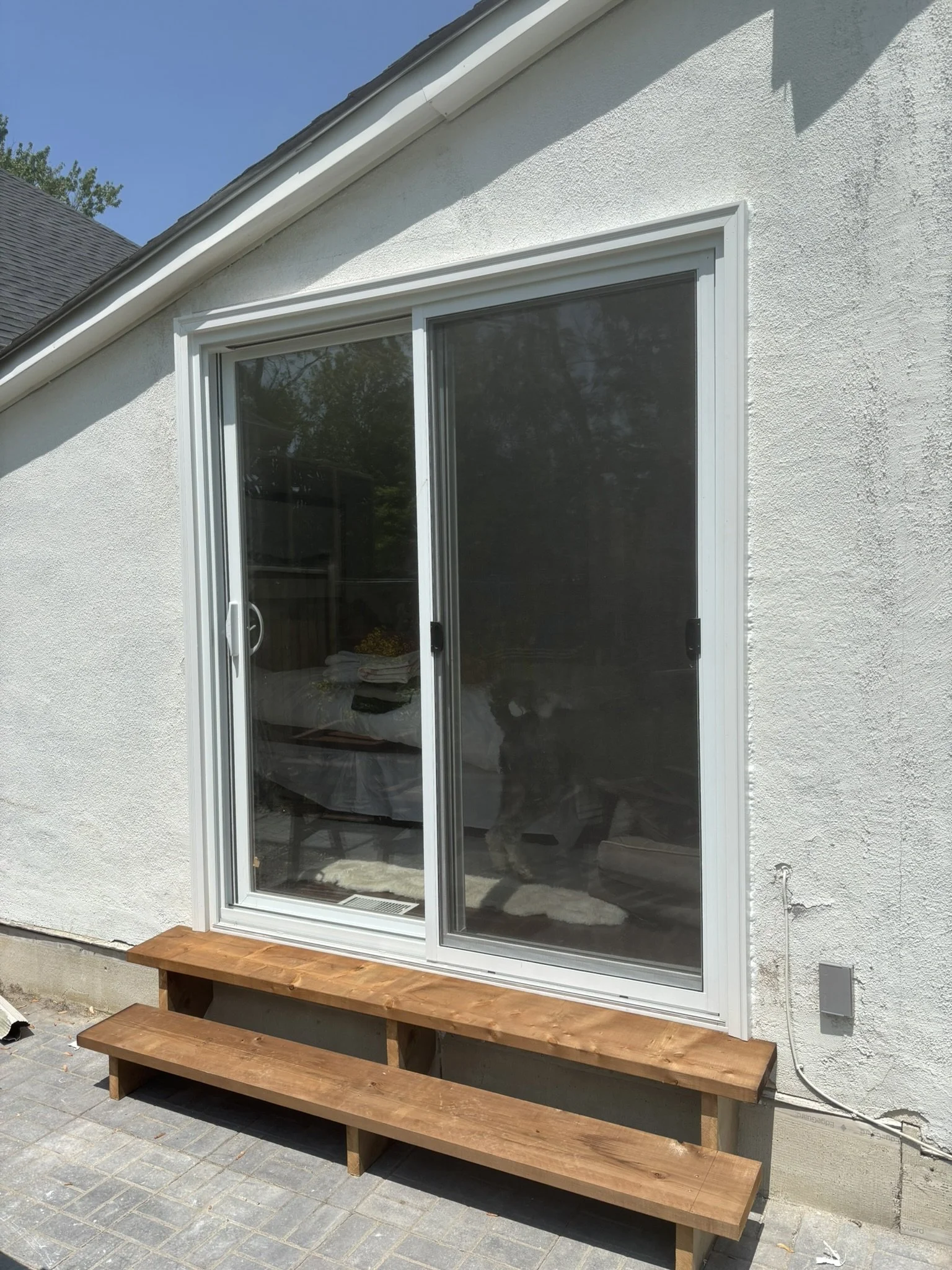 Front view of a sliding glass door with a newly constructed wooden step outside, attached to a white stucco house under a clear blue sky.