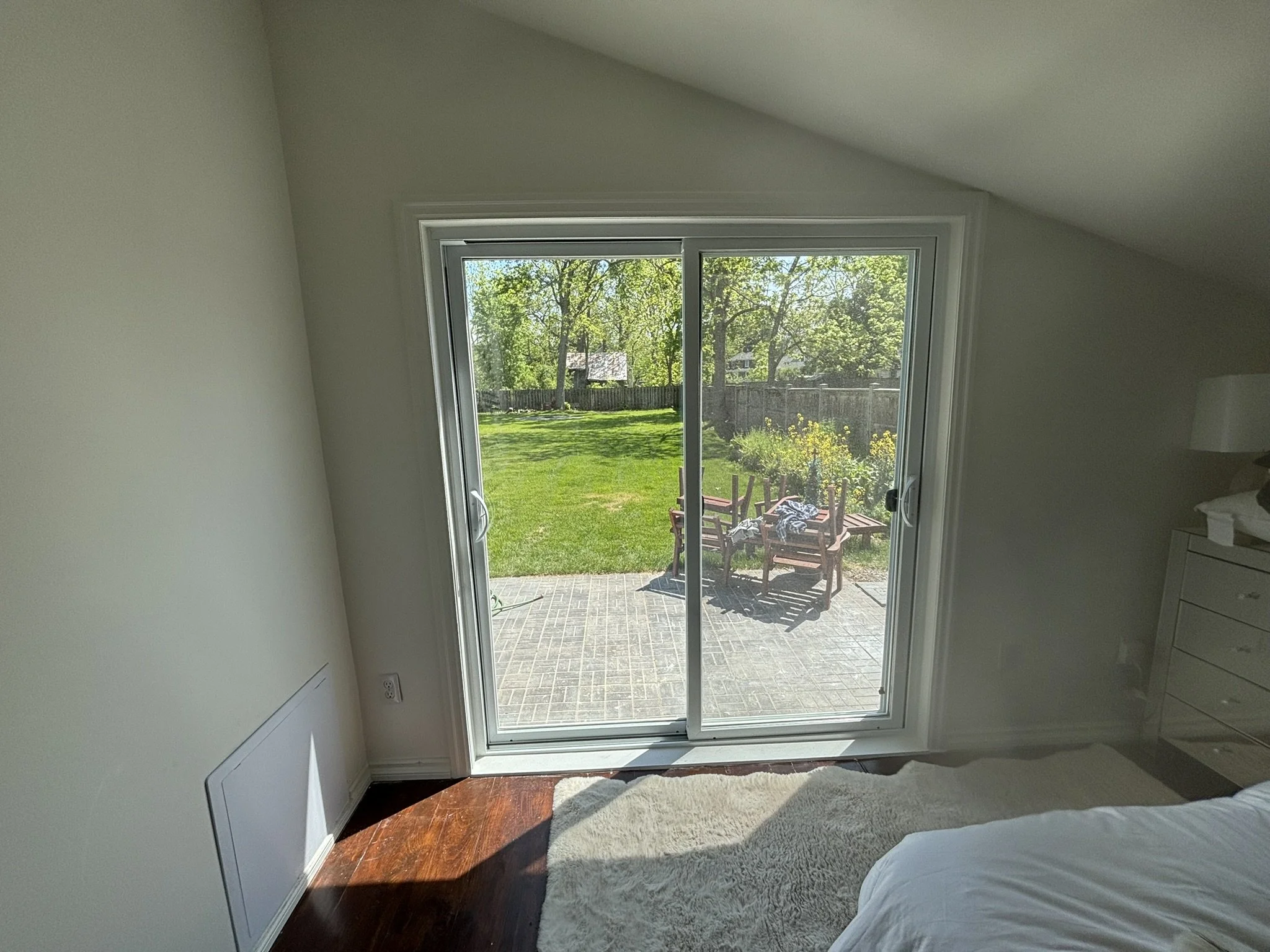 View of a backyard through sliding glass doors from inside a bedroom with a bed and dresser.