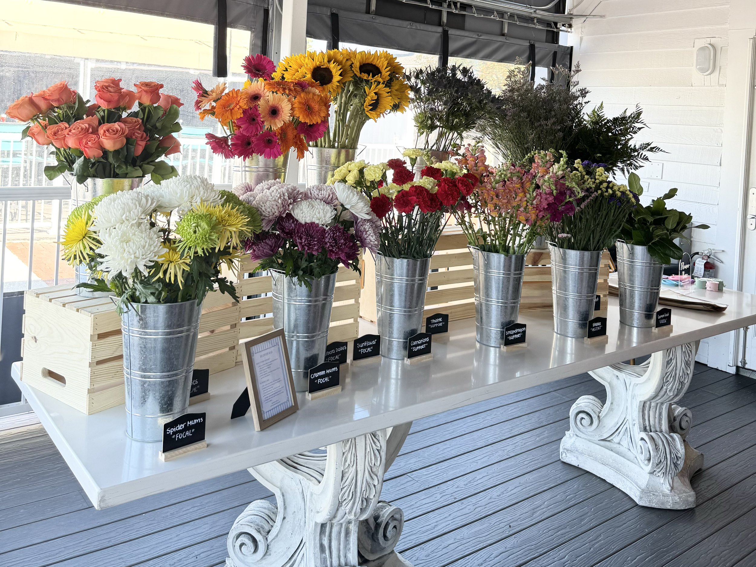 Display of colorful flowers in metal buckets on a white table with decorative white legs. Floral Flower Bouquet Bar.