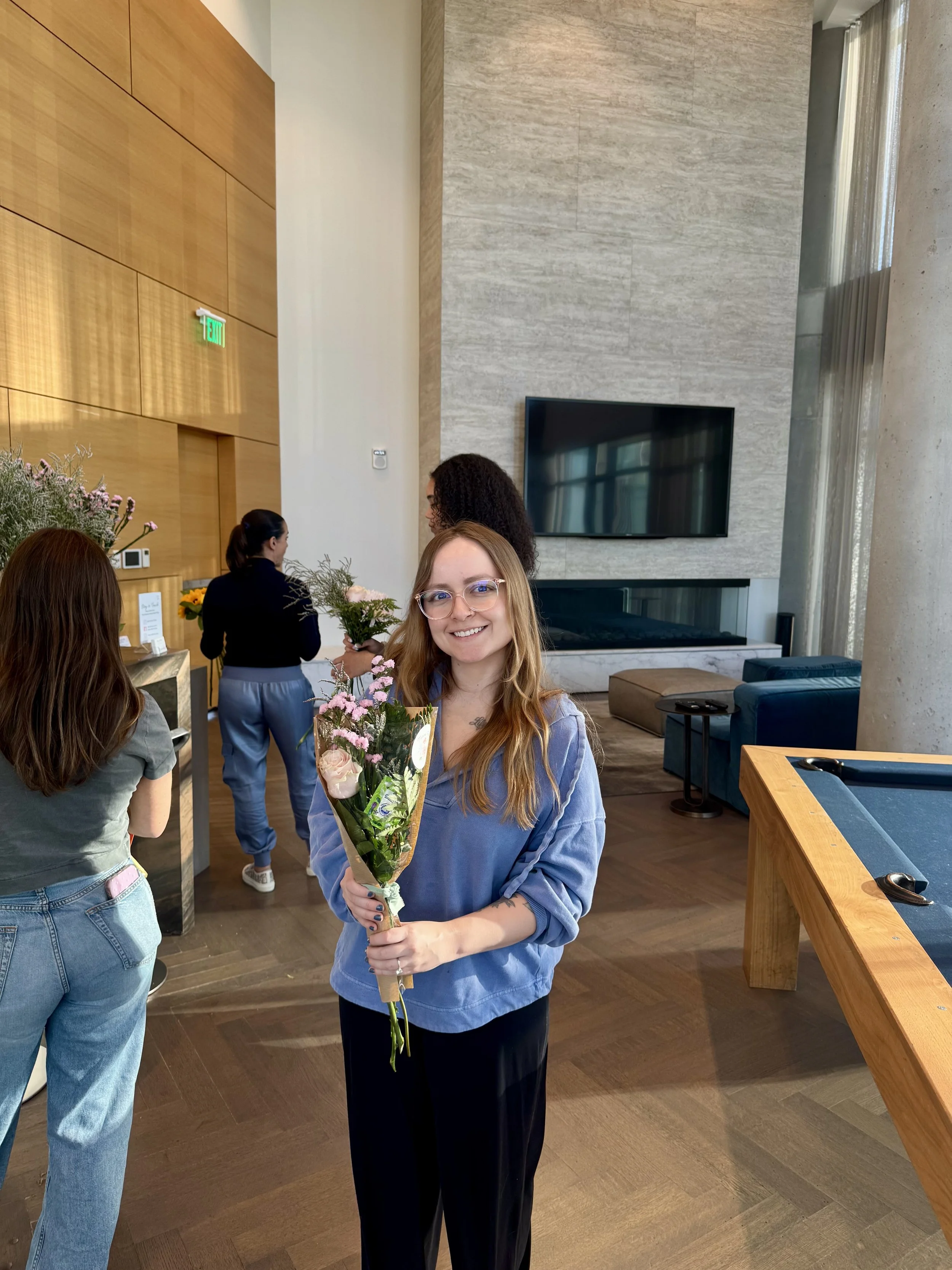 A smiling girl is holding a flowers in a wrapped bouquet that she put together from the flower bar event in her residential apartment building.