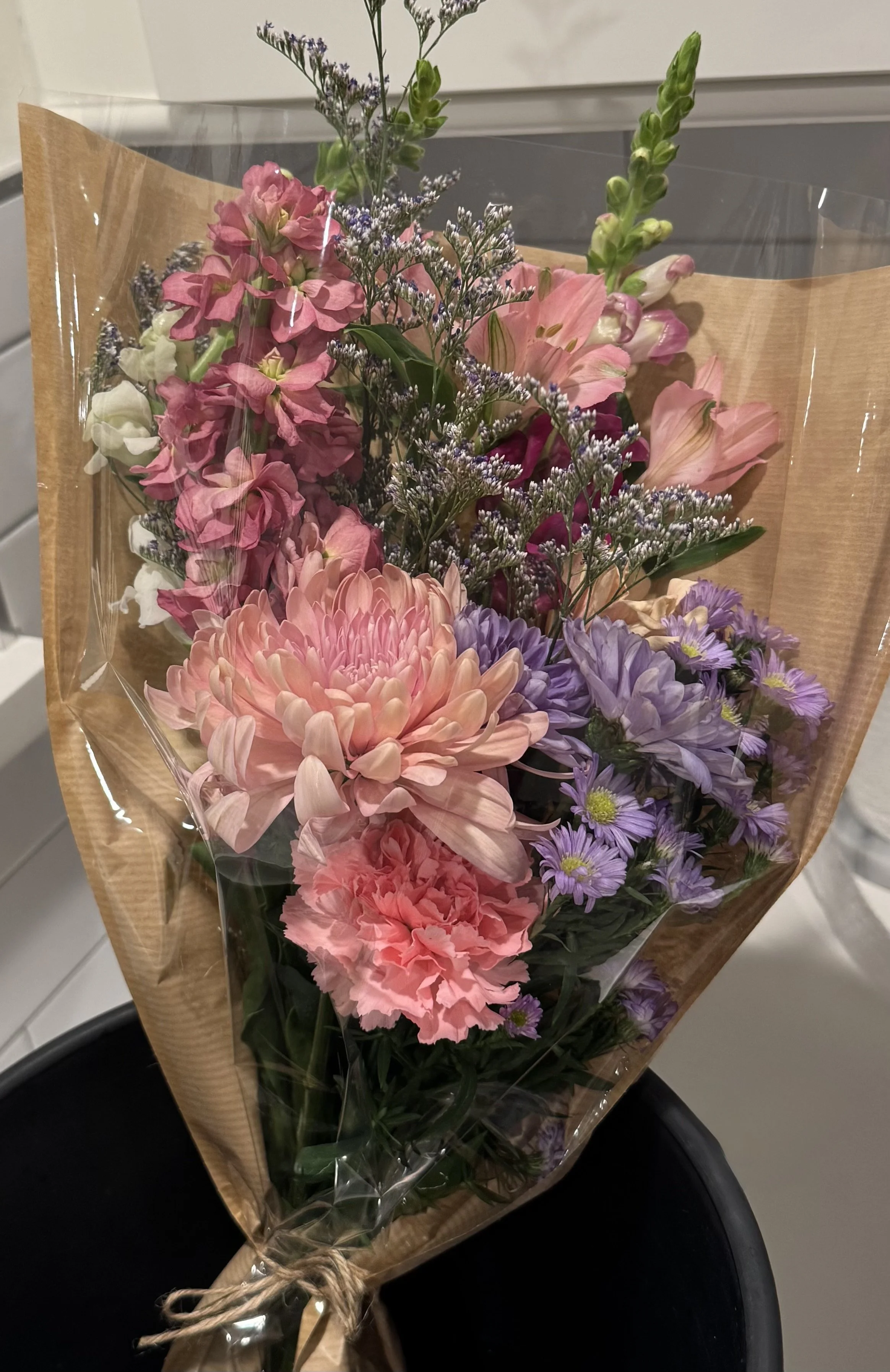 Bouquet of pink, purple, and white flowers wrapped in brown paper and clear plastic.