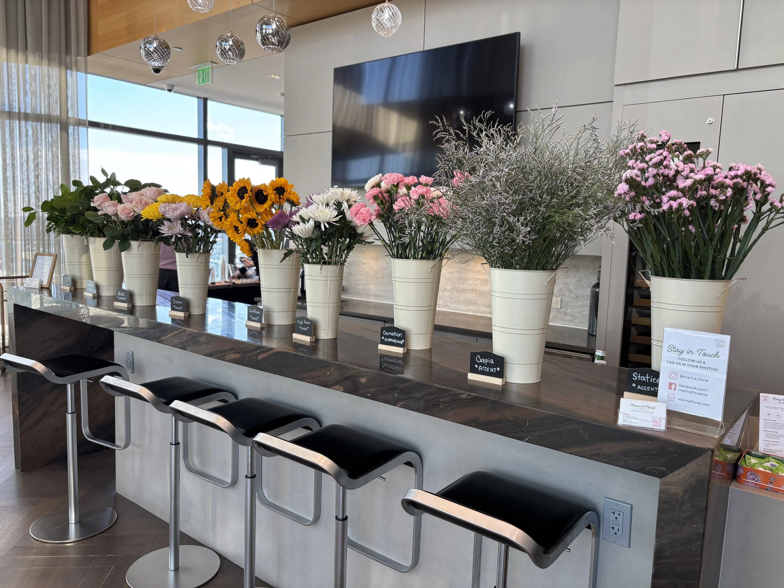 Flower bar set up with lots of different flowers and greenery in white metal buckets,  in a modern setting for a residential event in a luxury building. 
