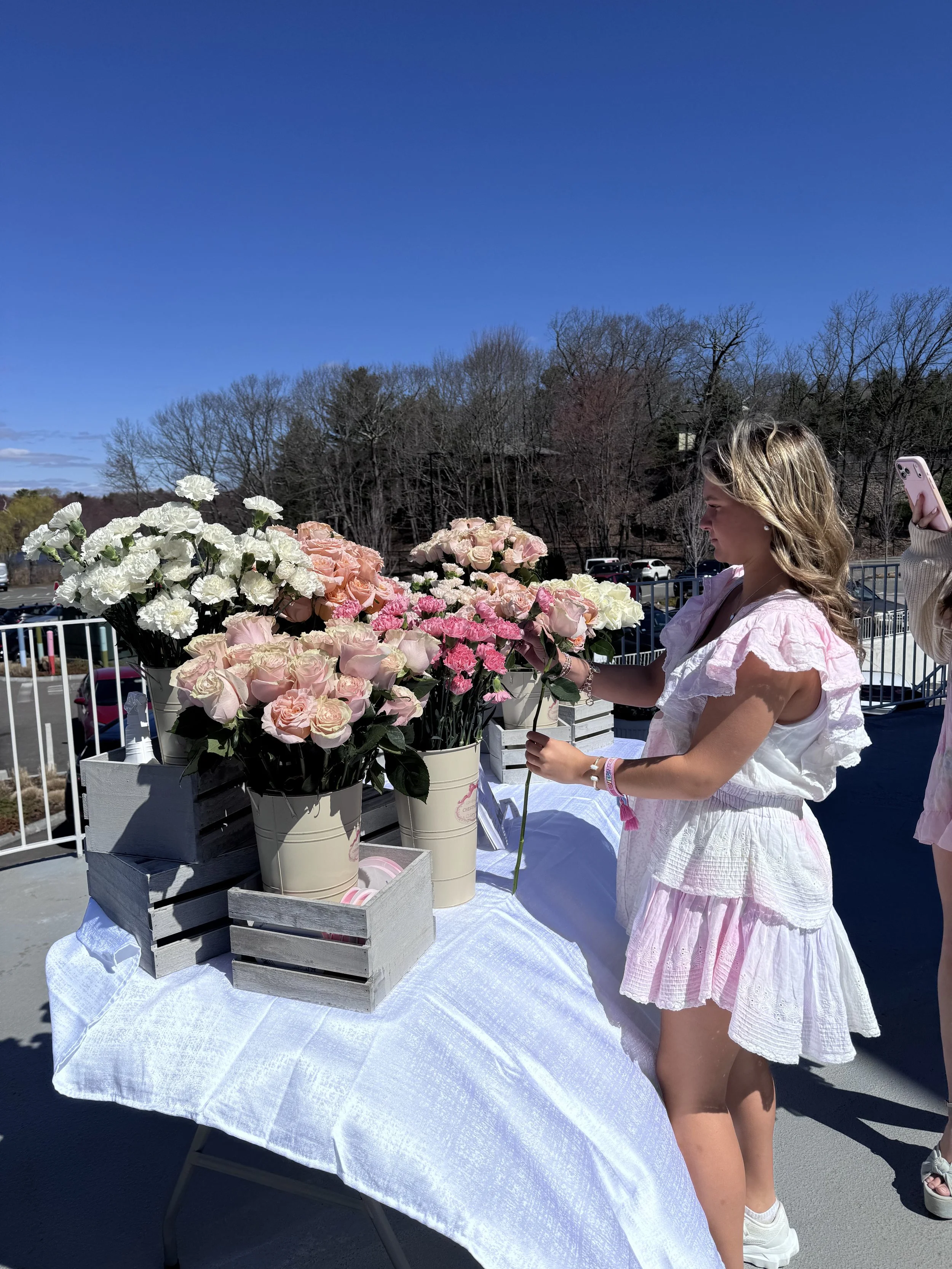 A girl in a LoveShackFancy pink dress is picking out her flowers to build her own DIY bouquet at a brand activation event with a flower bar.