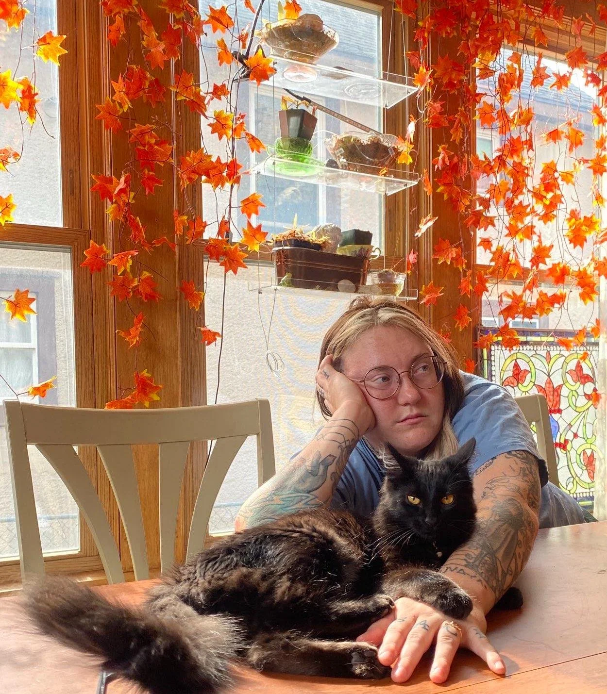 Nipinet sitting at a table with their arm wrapped around a black cat.