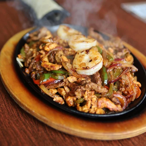 Sizzling beef and shrimp fajitas on a sizzling plate, garnished with colorful peppers and cooked onions